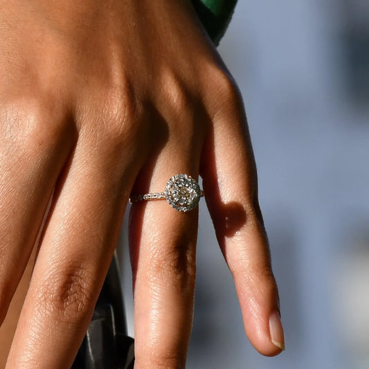 A person's hand holding a diamond ring in its finger.