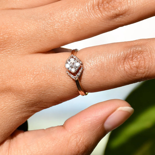 A person's hand displaying a gold ring with a central diamond surrounded by smaller diamonds set in a solid gold band.