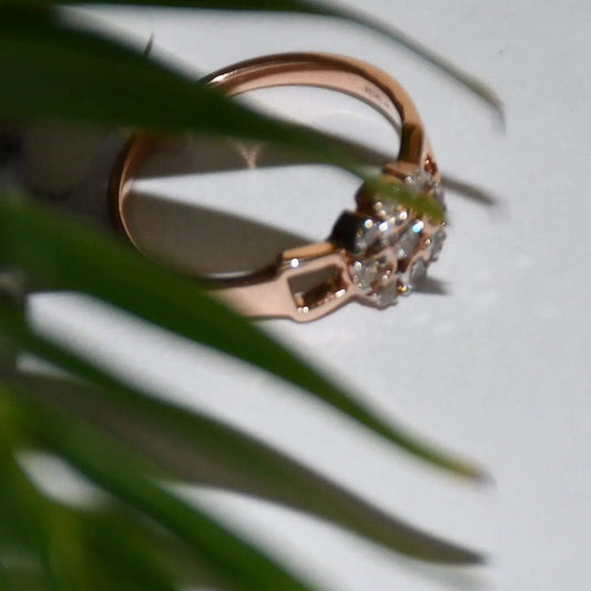 A 14K gold diamond band ring with a central row of diamonds and smaller surrounding diamonds set in a gold band displayed on a white surface and behind blur green leaves.