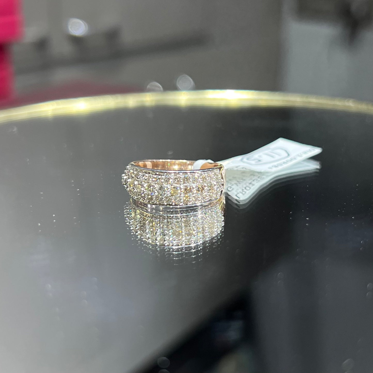 Close-up of a wide diamond band ring, featuring multiple rows of sparkling round-cut diamonds set in gold, displayed on a reflective surface.