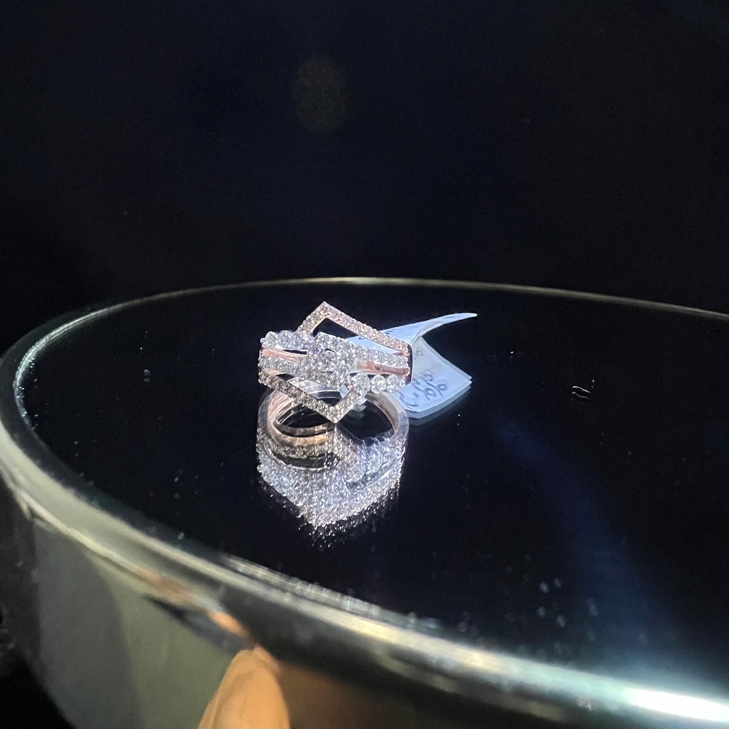 A gold band ring with central diamonds, surrounded by smaller diamonds set in the band is displayed on a reflective surface.