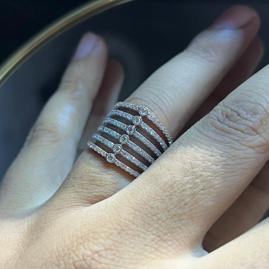 Close-up of a hand wearing a modern multi-band diamond ring featuring parallel pavé-set rows connected by bezel-set round diamonds, crafted in gold and reflecting light beautifully.