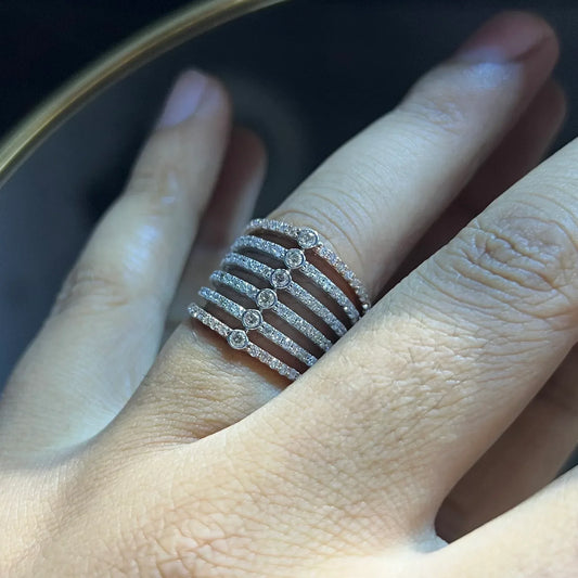 Close-up of a hand wearing a modern multi-band diamond ring featuring parallel pavé-set rows connected by bezel-set round diamonds, crafted in gold and reflecting light beautifully.