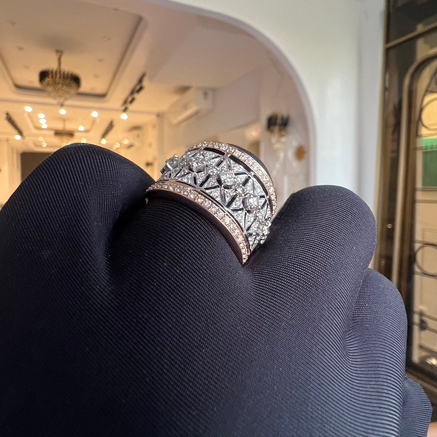 A ring with a band-style design, featuring a central diamond surrounded by smaller diamonds set in a gold band, displayed by a hand.