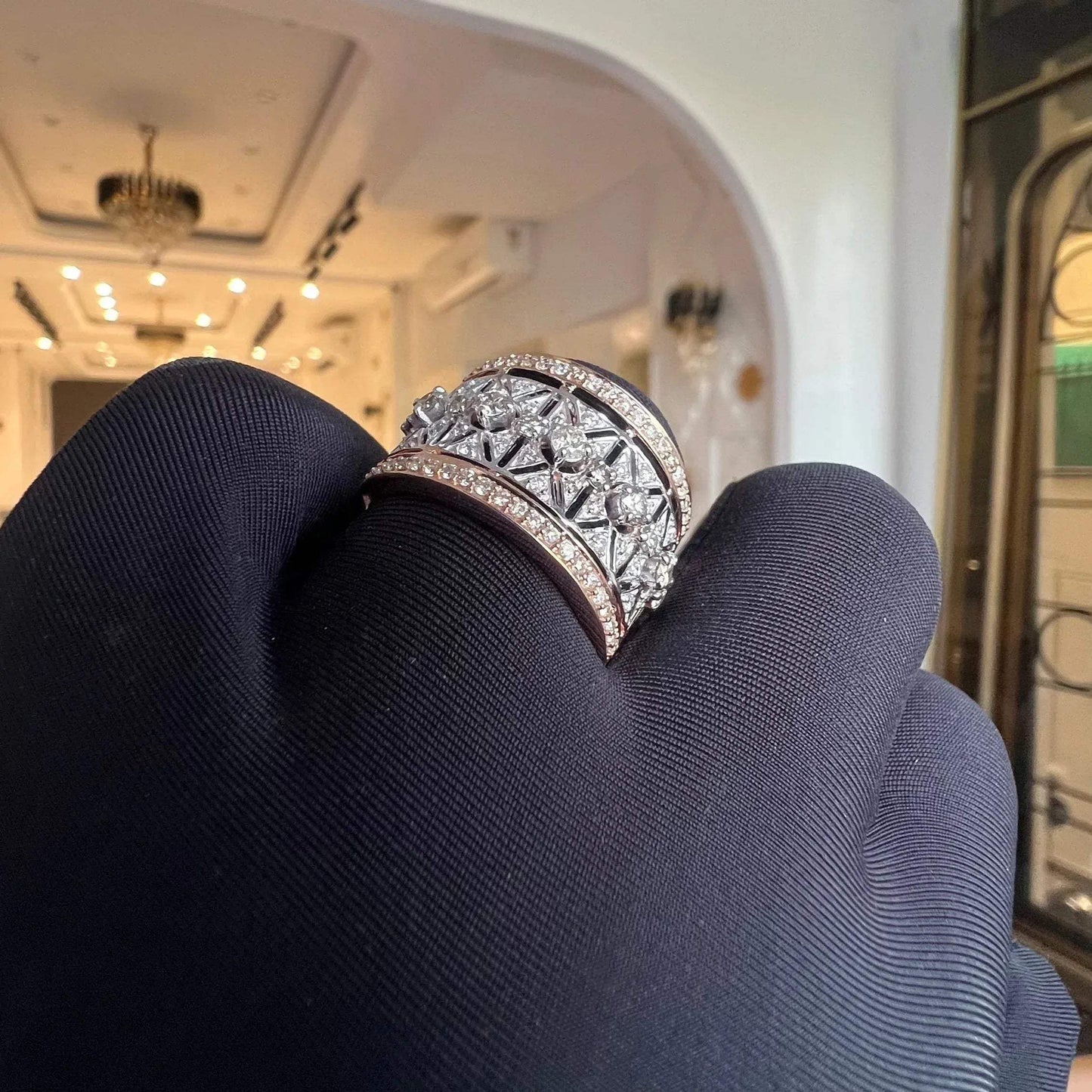 A ring with a band-style design, featuring a central diamond surrounded by smaller diamonds set in a gold band, displayed by a hand.