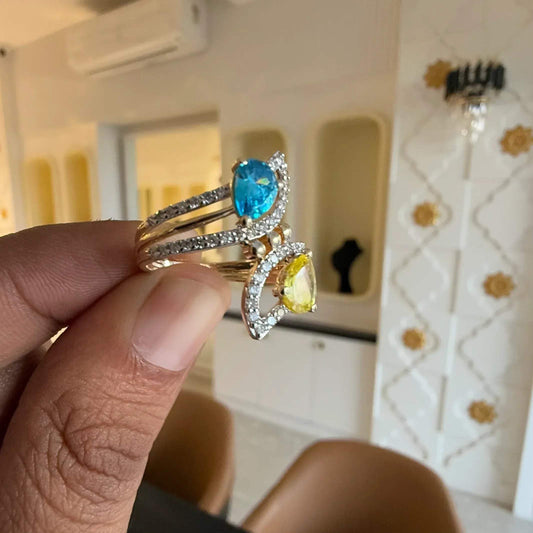 A person's hand displaying a two-stone diamond ring with yellow and blue colors, made of 14kt gold.
