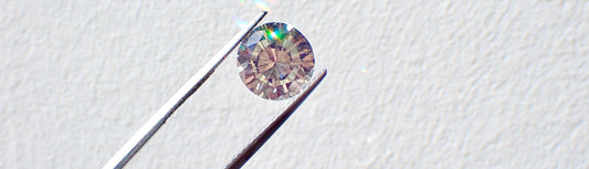 Lab grown diamond held by tweezers on a light gray background