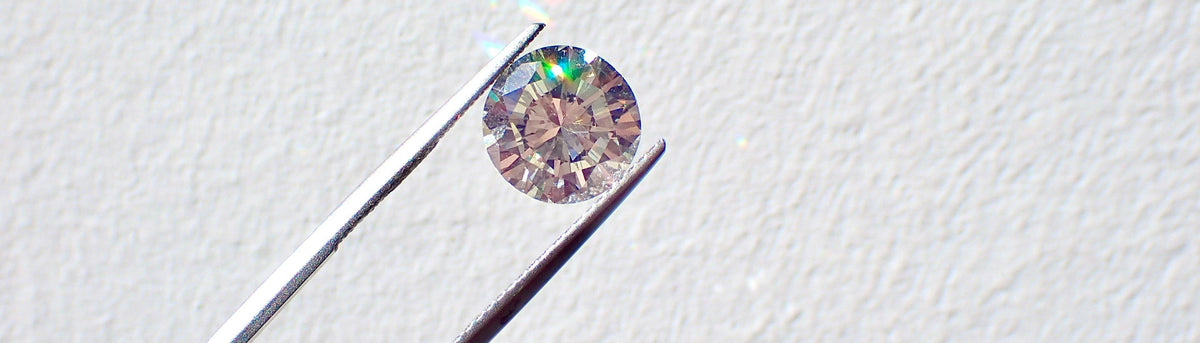 Lab grown diamond held by tweezers on a light gray background