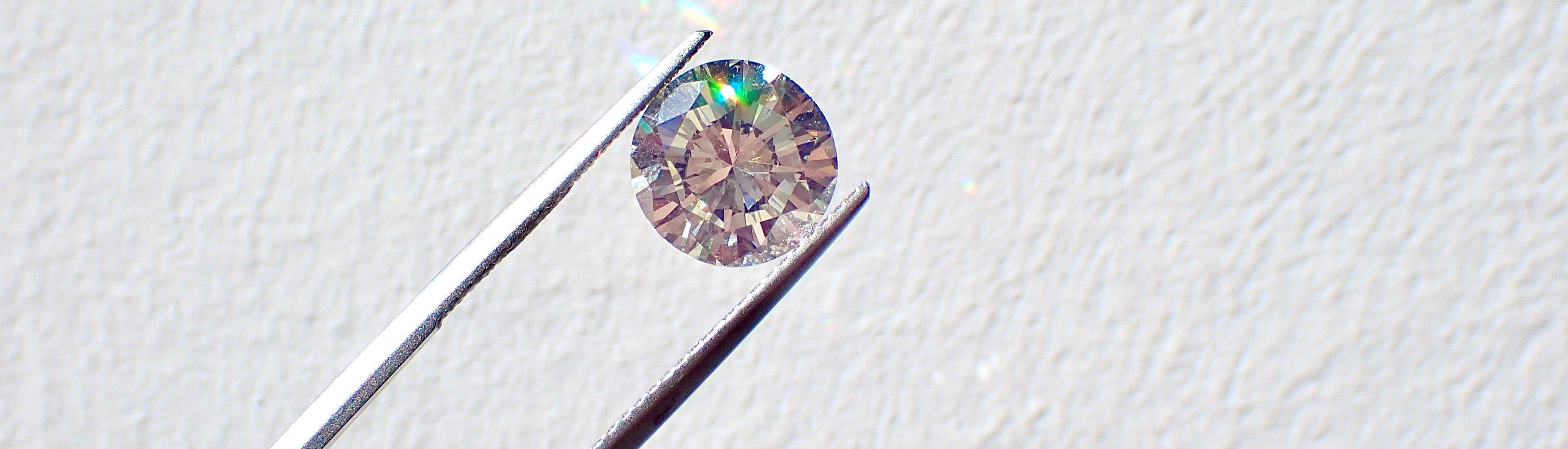 Lab grown diamond held by tweezers on a light gray background