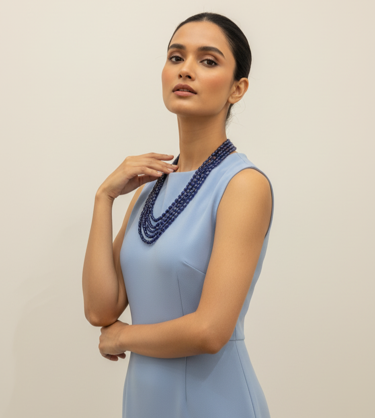 Woman wearing a light blue dress with a beaded necklace against a plain background