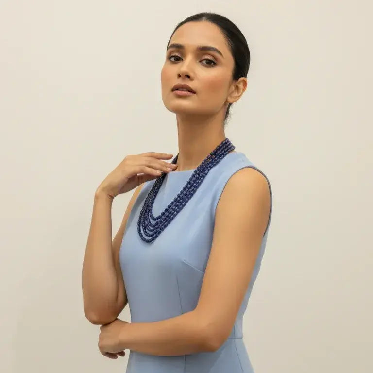 Woman wearing a light blue dress with a beaded necklace against a plain background