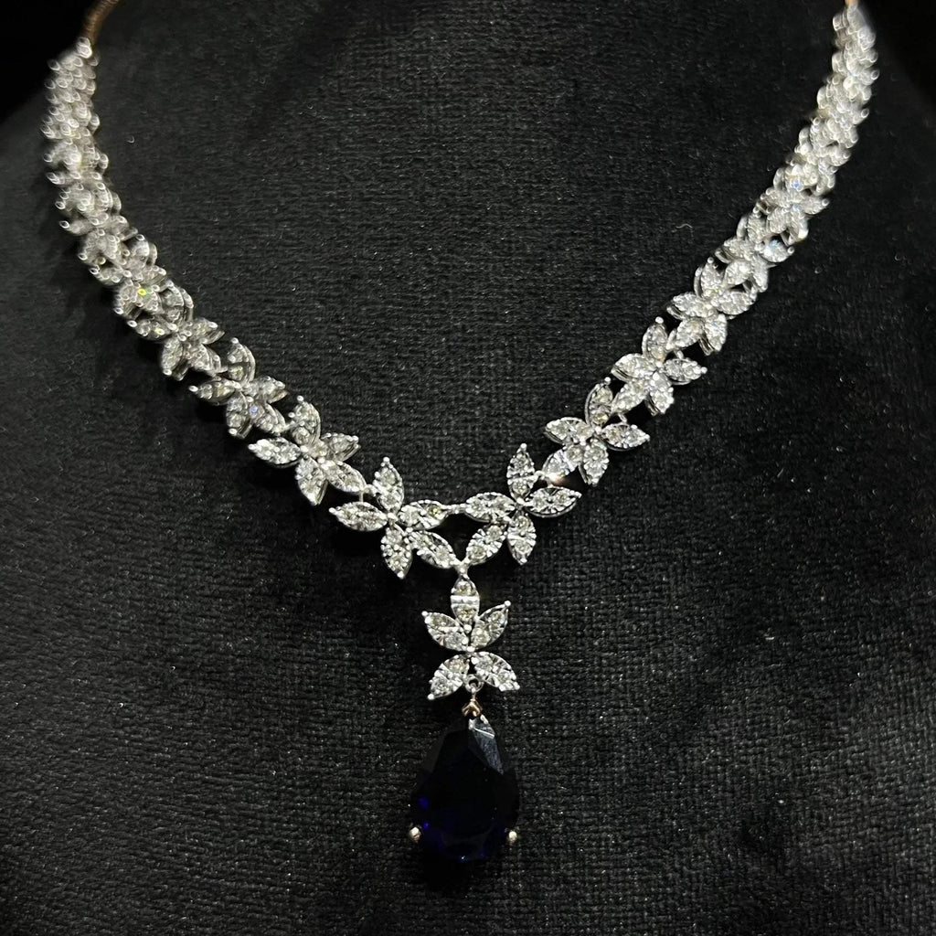 Close-up of diamond necklace set showing detailed floral design and pear-shaped color stone drop pendant on a mannequin bust.