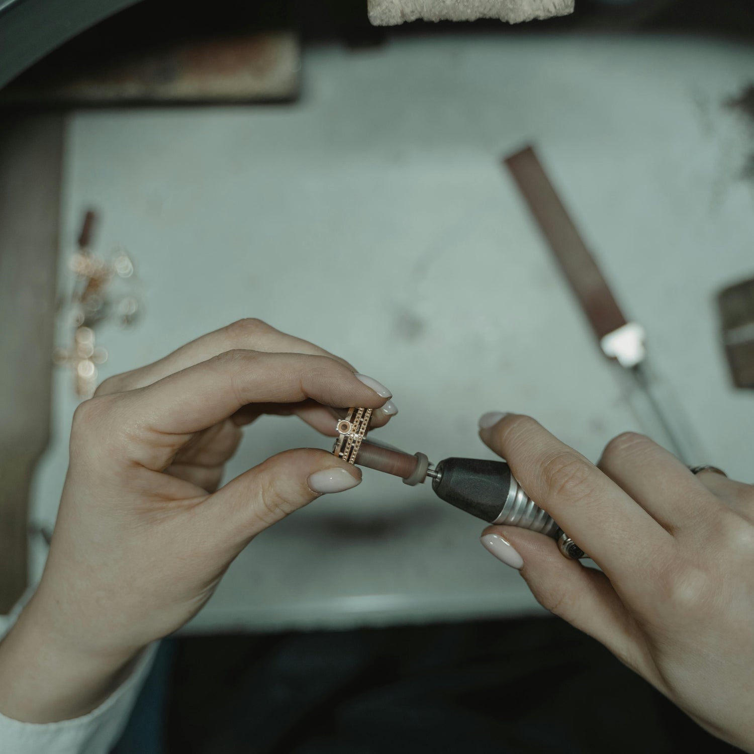 Person working on a small jewelry piece with tools on a table.