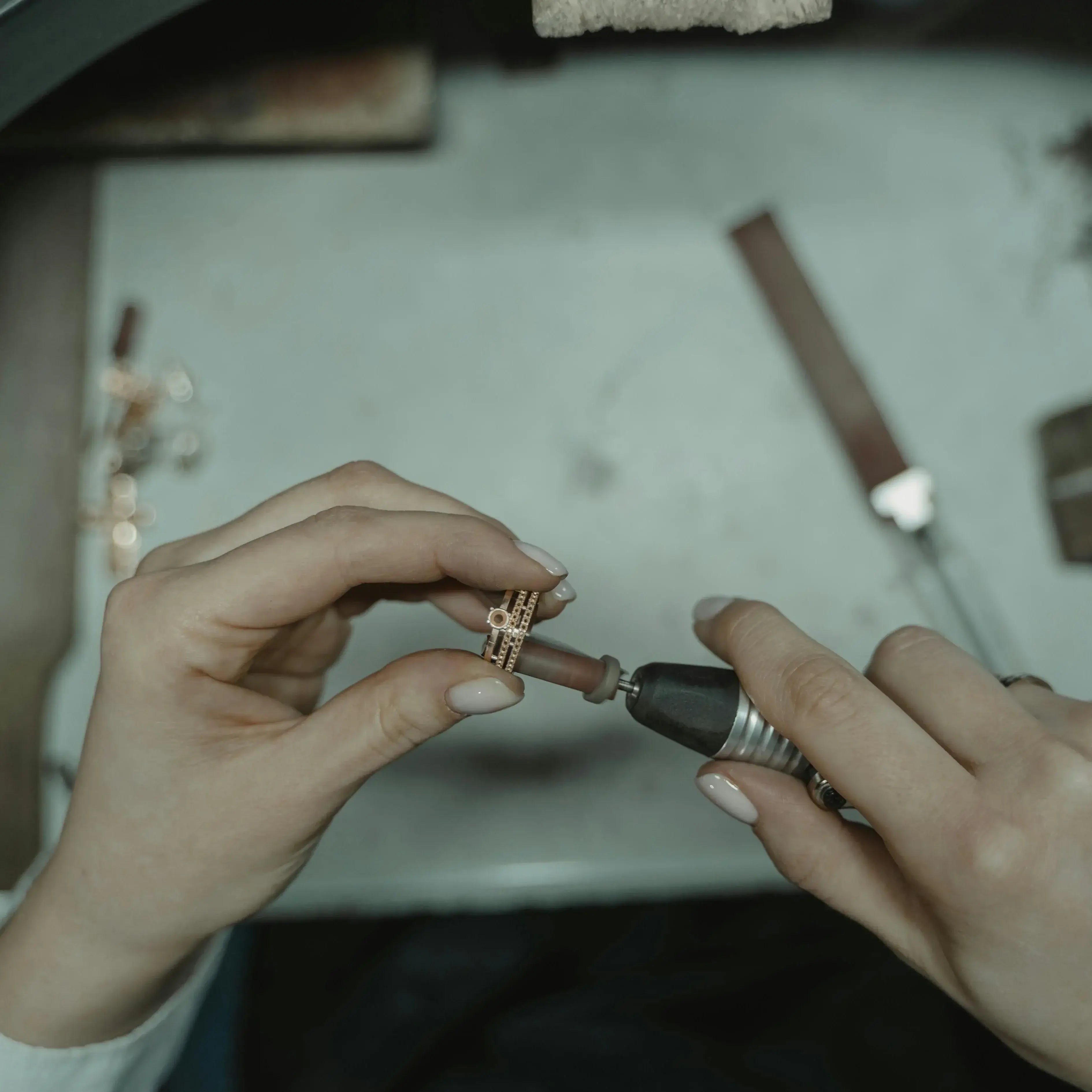 Person working on a small jewelry piece with tools on a table.