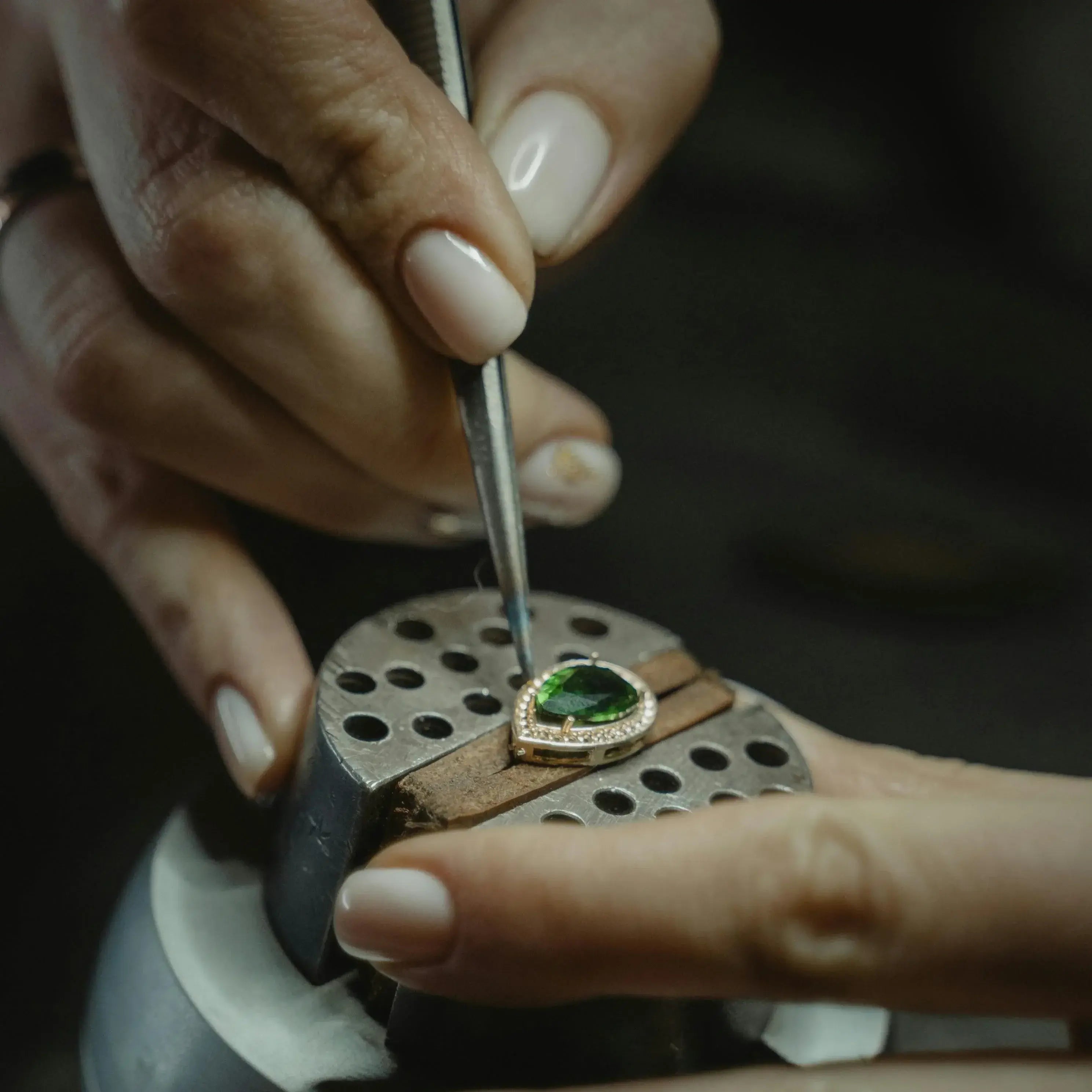 Person working on a piece of jewelry with a green gemstone using a tool.