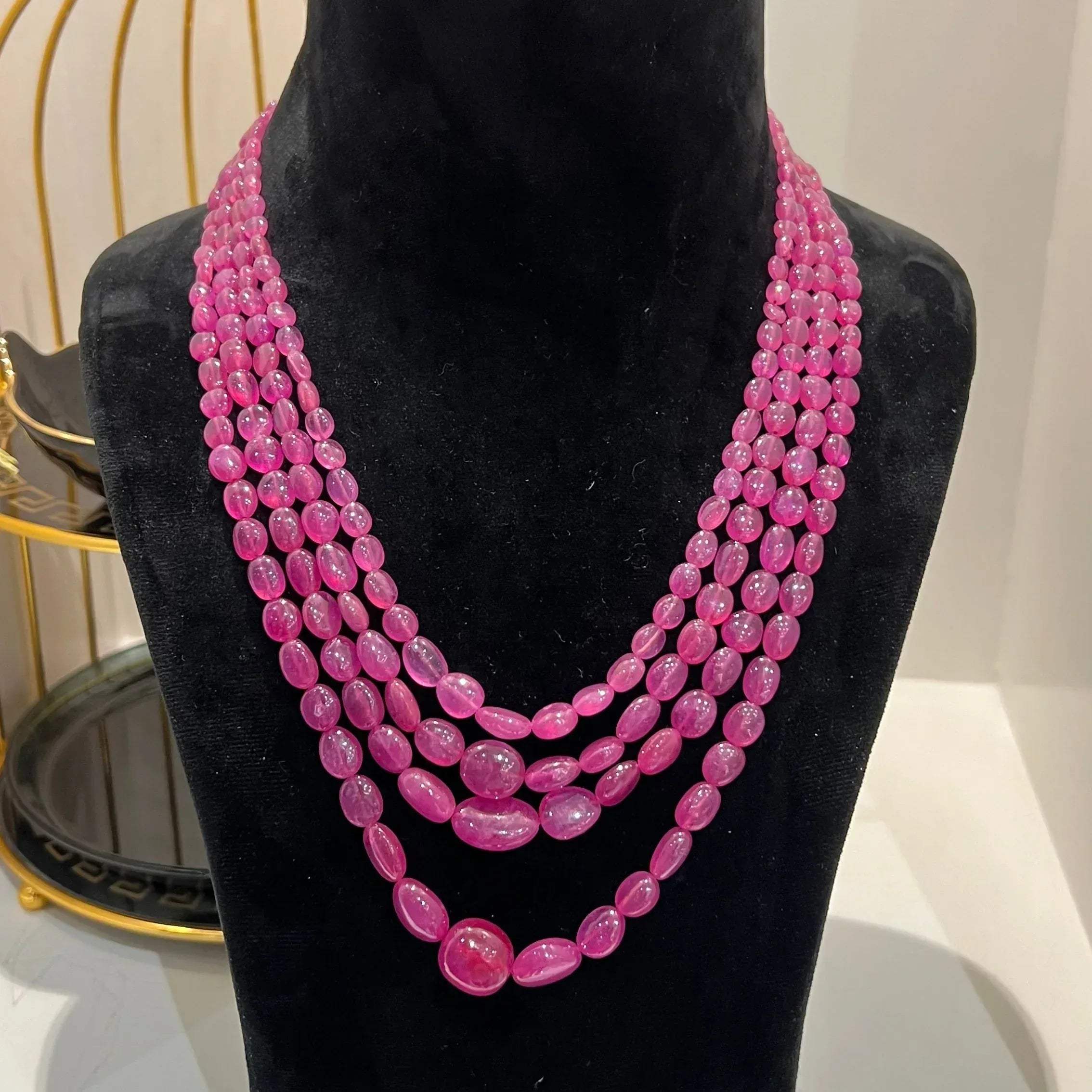 A black mannequin necklace displaying a multi-layered pink ruby beaded necklace with adjustable Dori.