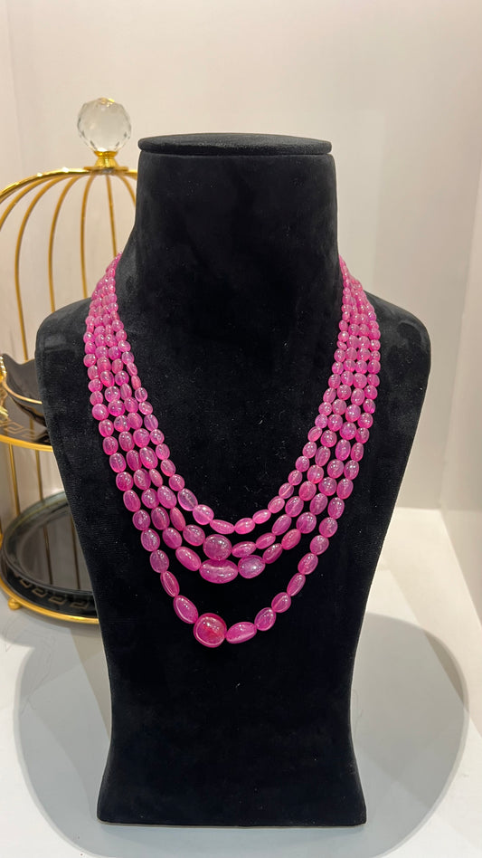 A black mannequin necklace displaying a multi-layered pink ruby beaded necklace with adjustable Dori.