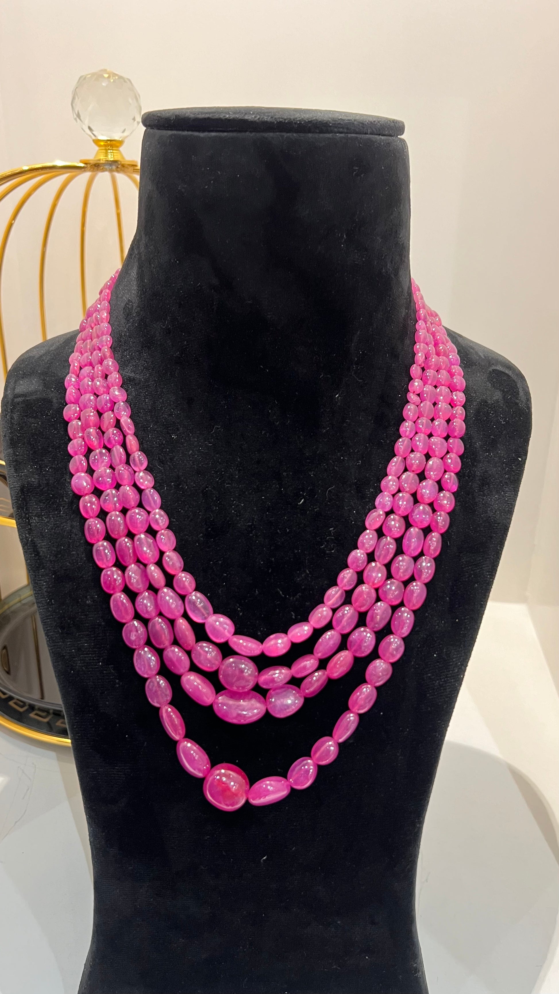 A black mannequin necklace displaying a multi-layered pink ruby beaded necklace with adjustable Dori.