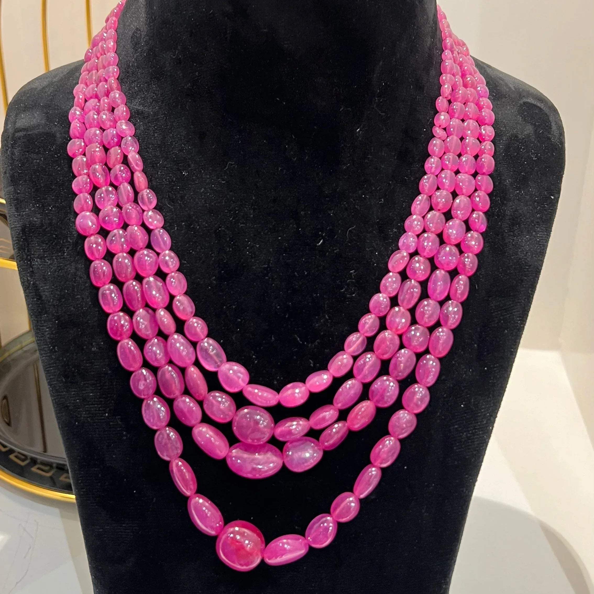 A black mannequin necklace displaying a multi-layered pink ruby beaded necklace with adjustable Dori.