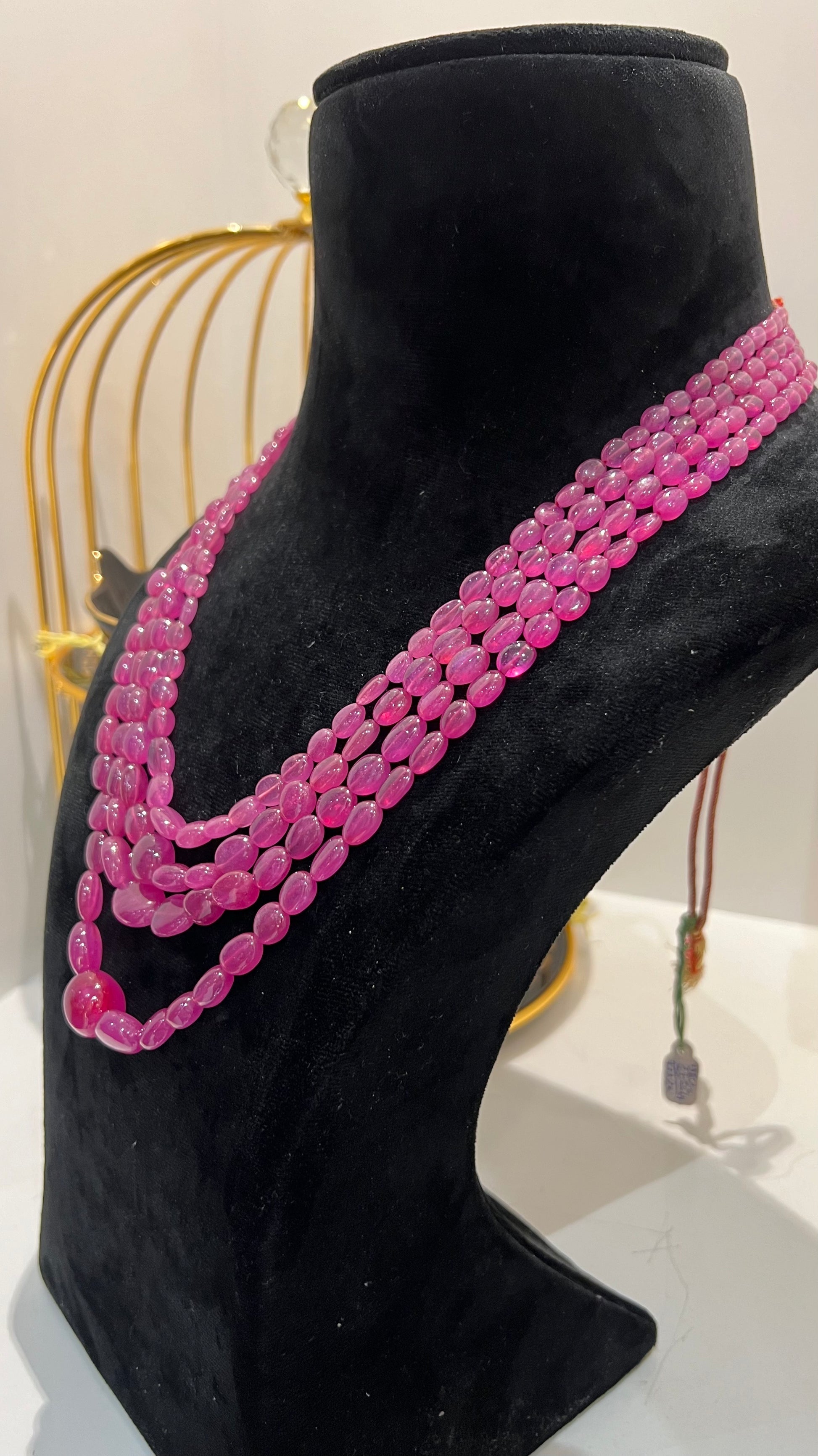 A black mannequin necklace displaying a multi-layered pink ruby beaded necklace with adjustable Dori.