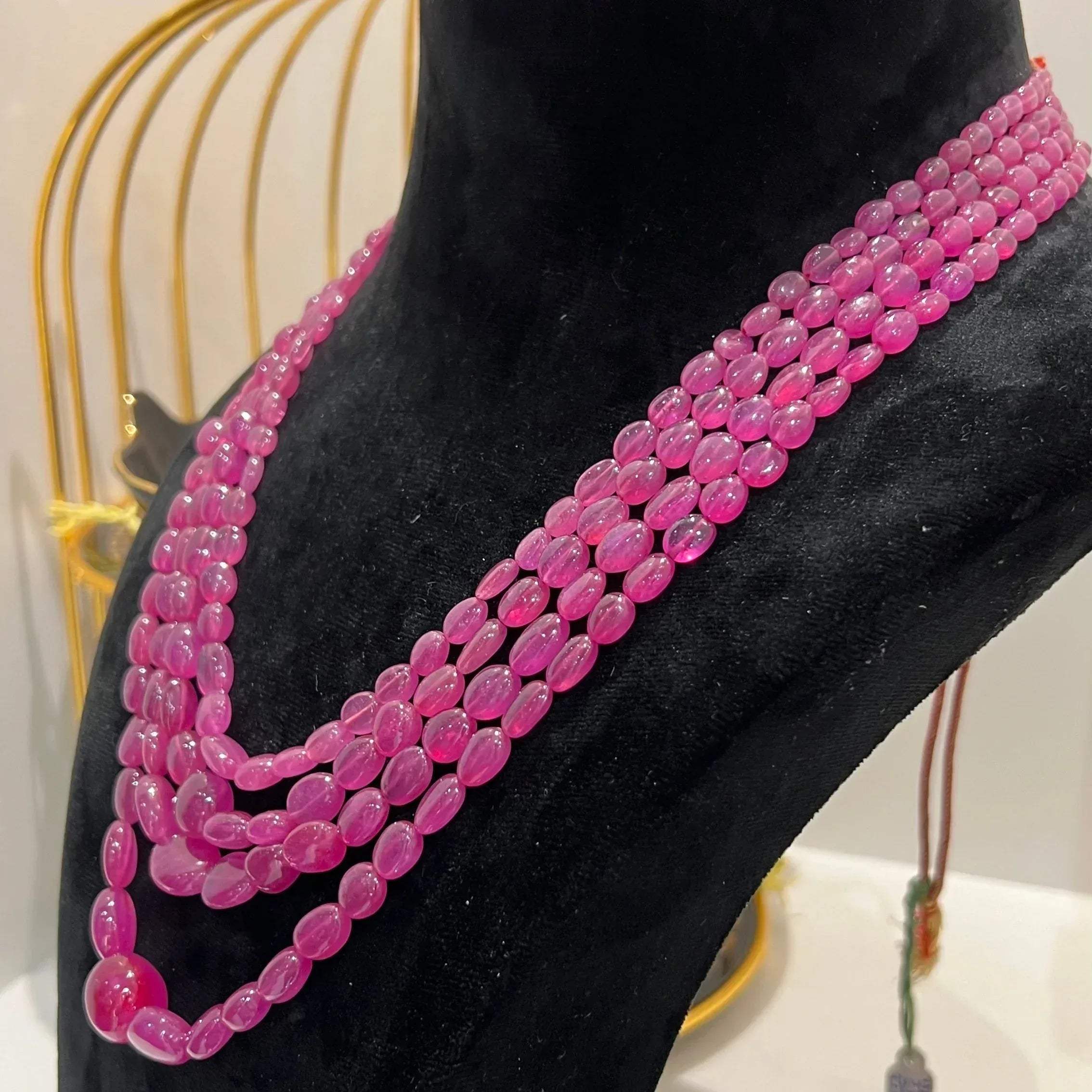 A black mannequin necklace displaying a multi-layered pink ruby beaded necklace with adjustable Dori.