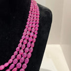 A black mannequin necklace displaying a multi-layered pink ruby beaded necklace with adjustable Dori.
