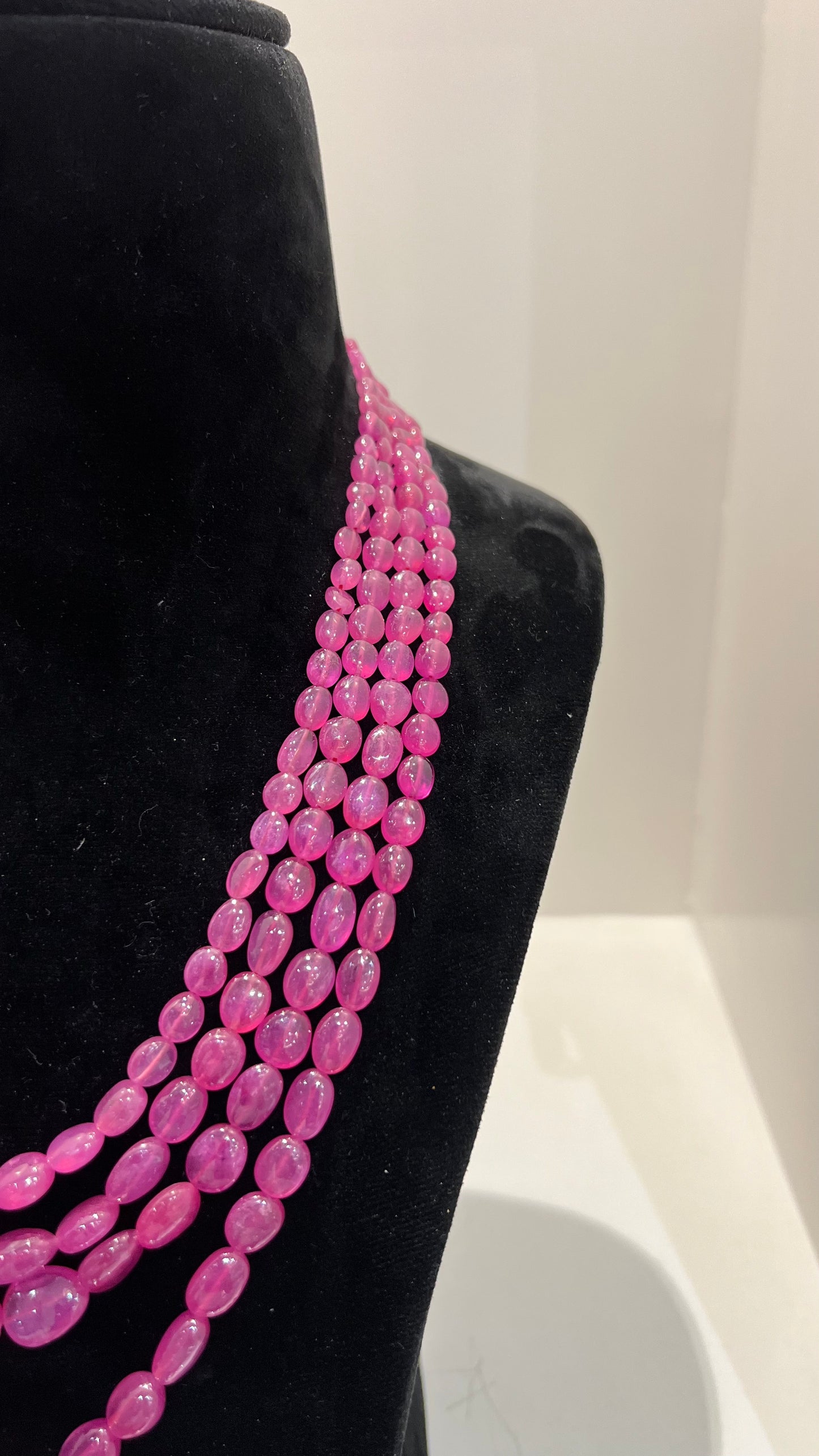 A black mannequin necklace displaying a multi-layered pink ruby beaded necklace with adjustable Dori.