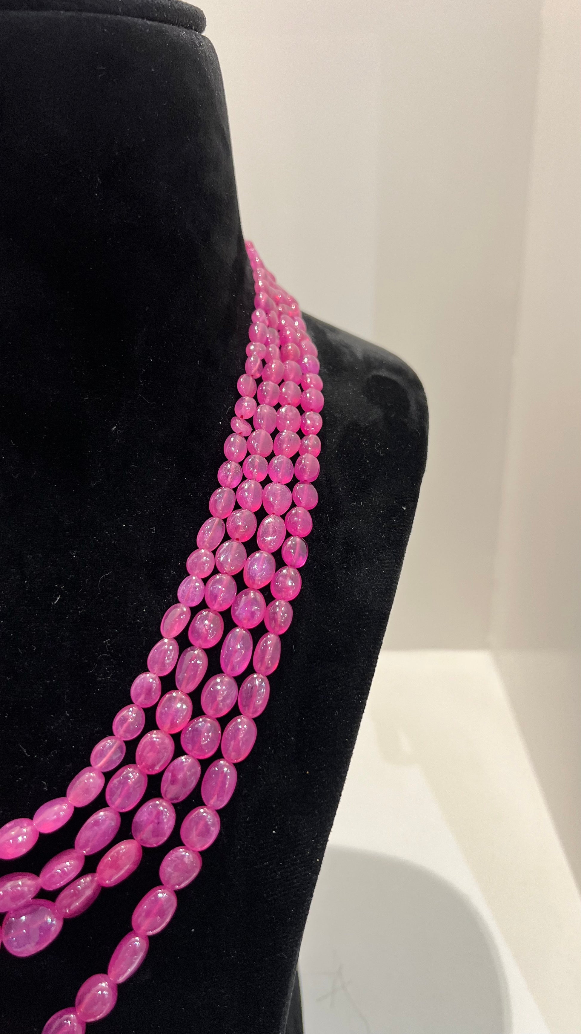 A black mannequin necklace displaying a multi-layered pink ruby beaded necklace with adjustable Dori.