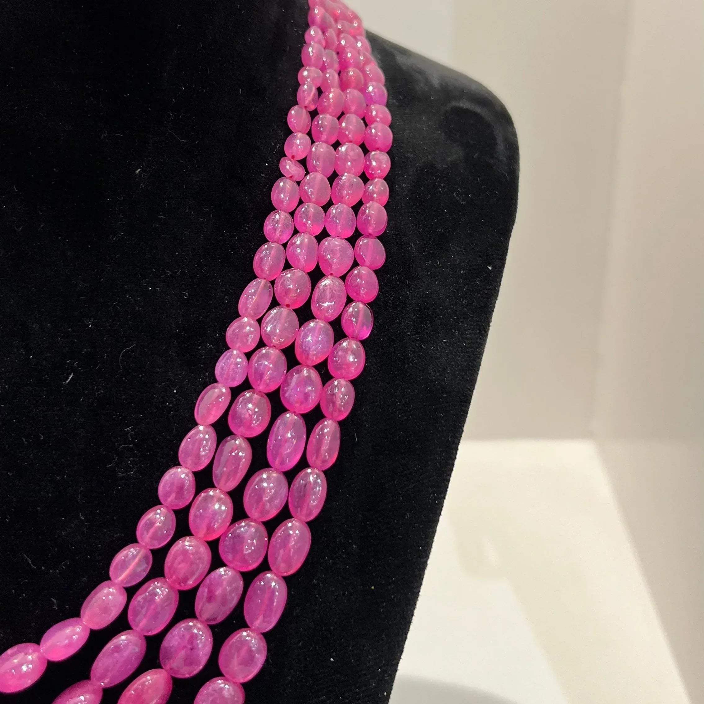 A black mannequin necklace displaying a multi-layered pink ruby beaded necklace with adjustable Dori.