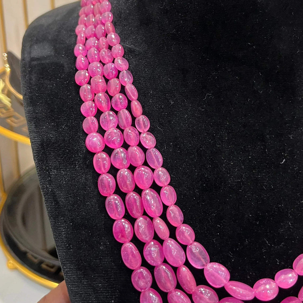 A black mannequin necklace displaying a multi-layered pink ruby beaded necklace with adjustable Dori.