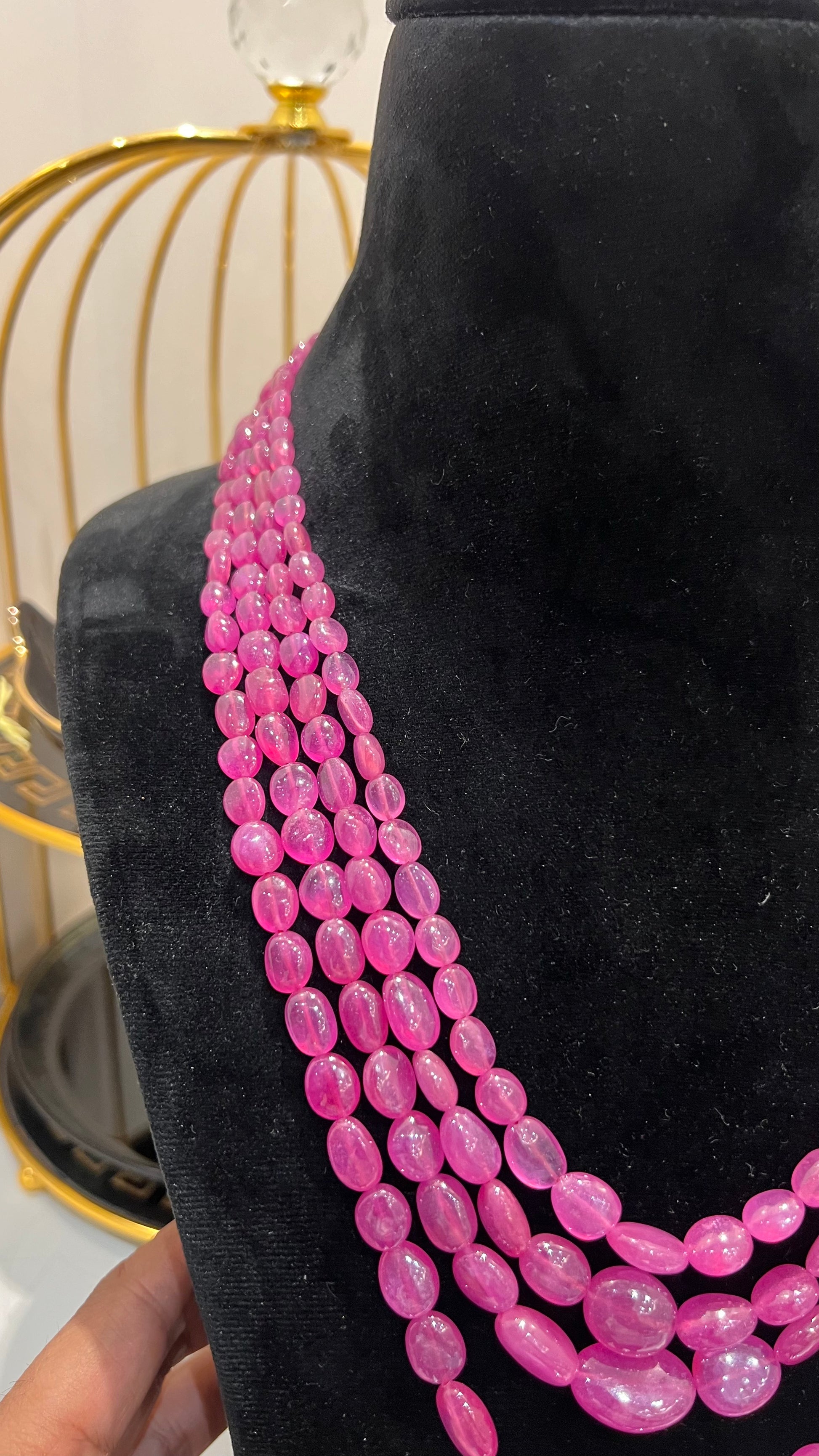 A black mannequin necklace displaying a multi-layered pink ruby beaded necklace with adjustable Dori.