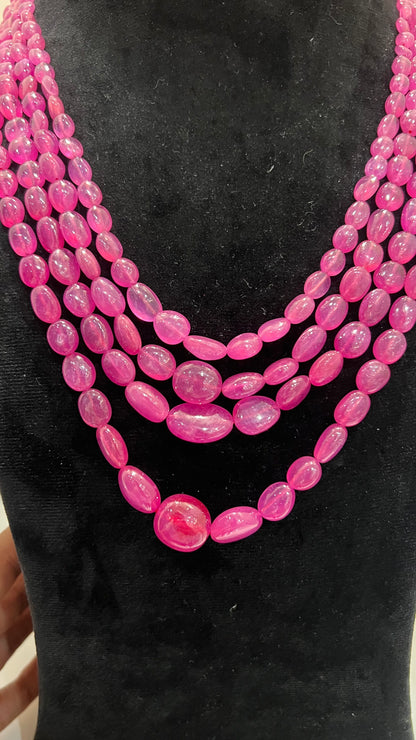 A black mannequin necklace displaying a multi-layered pink ruby beaded necklace with adjustable Dori.