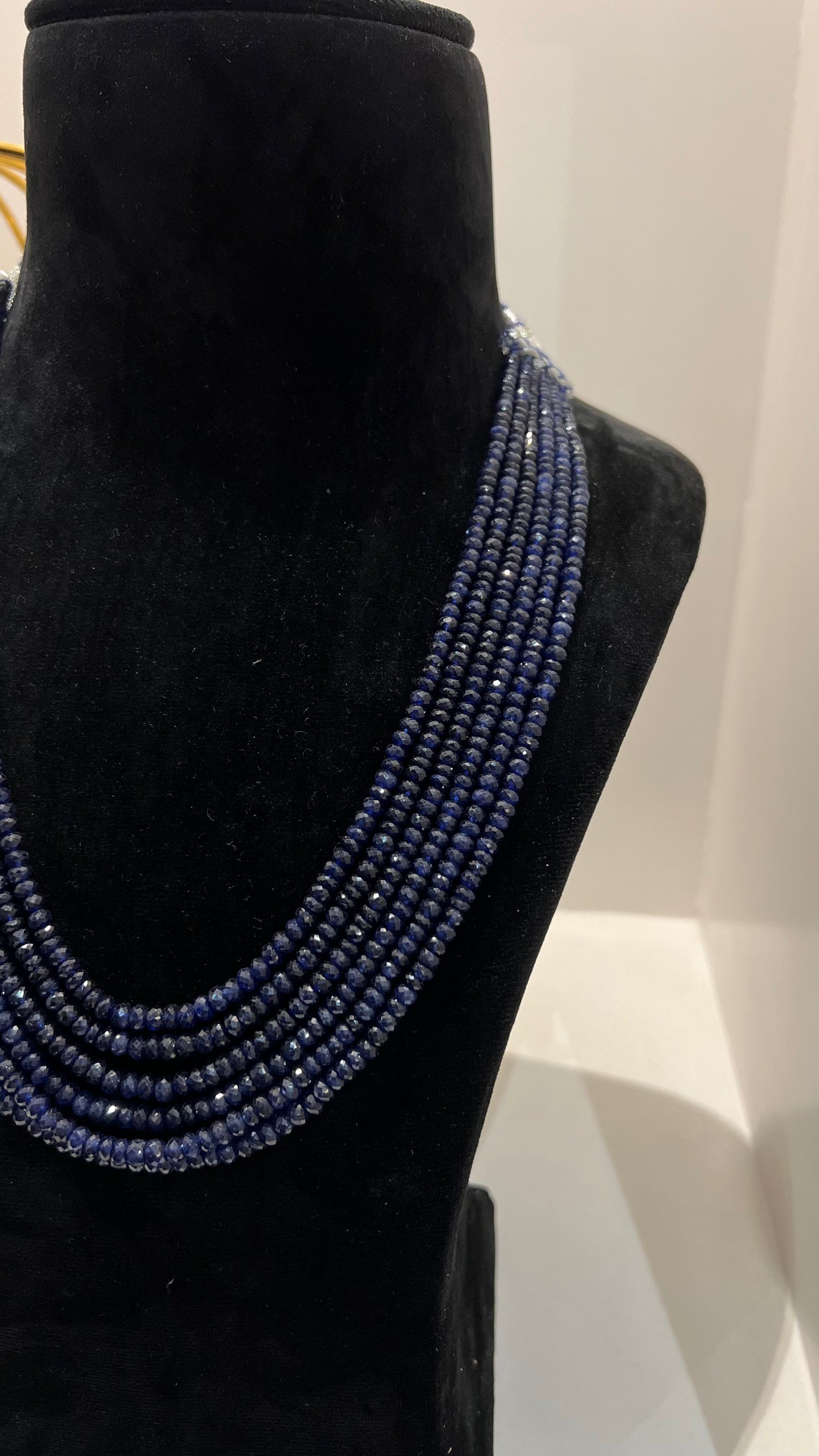 A multi-strand 6 layer blue sapphire beads necklace displayed on a black mannequin bust.
