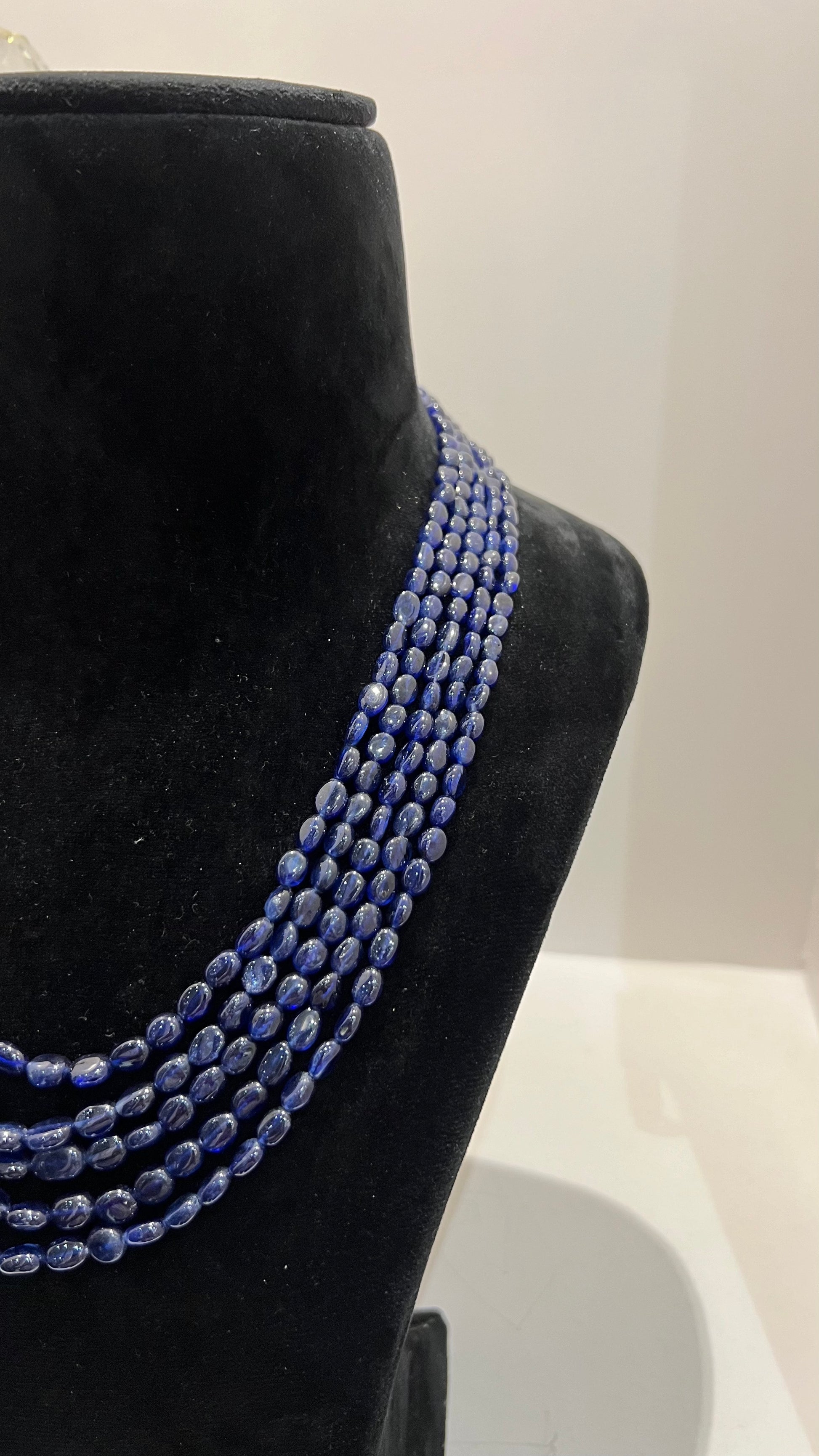A multi-strand 5 layer blue sapphire beads necklace displayed on a mannequinnecklace stand.
