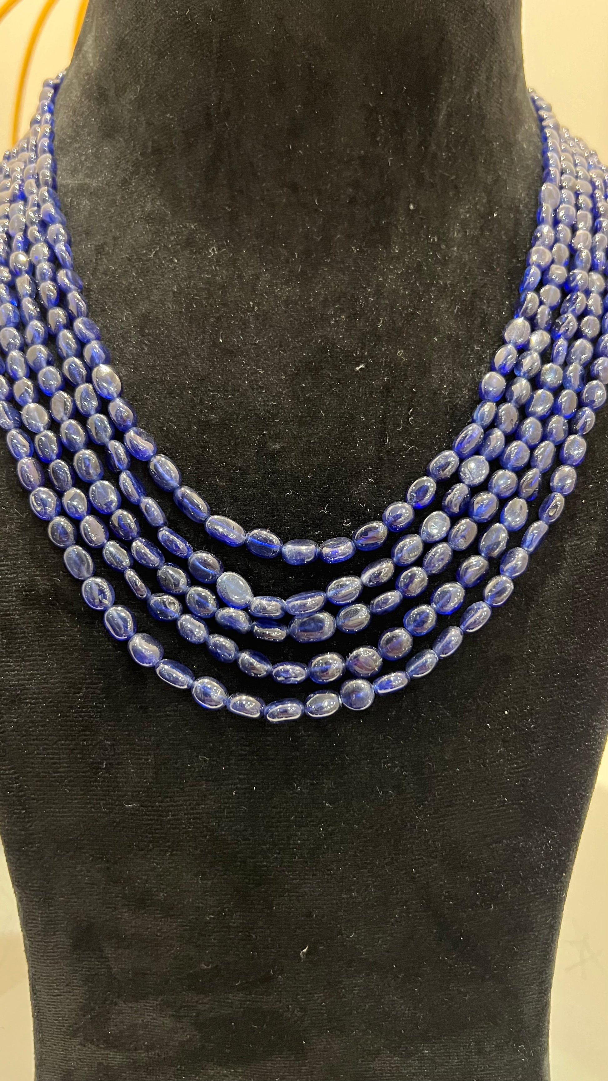 A multi-strand 5 layer blue sapphire beads necklace displayed on a mannequinnecklace stand.