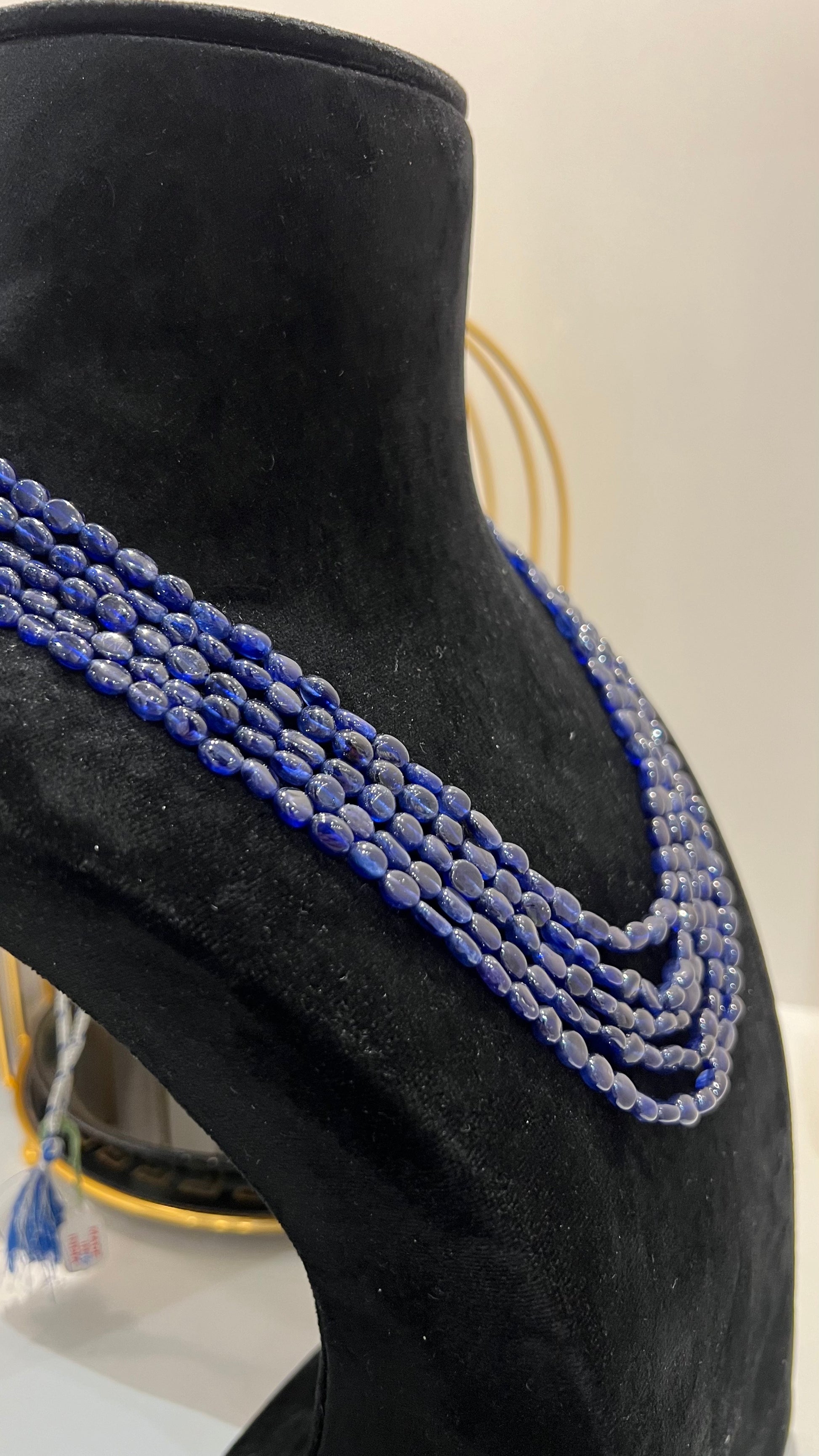 A multi-strand 5 layer blue sapphire beads necklace displayed on a mannequinnecklace stand.