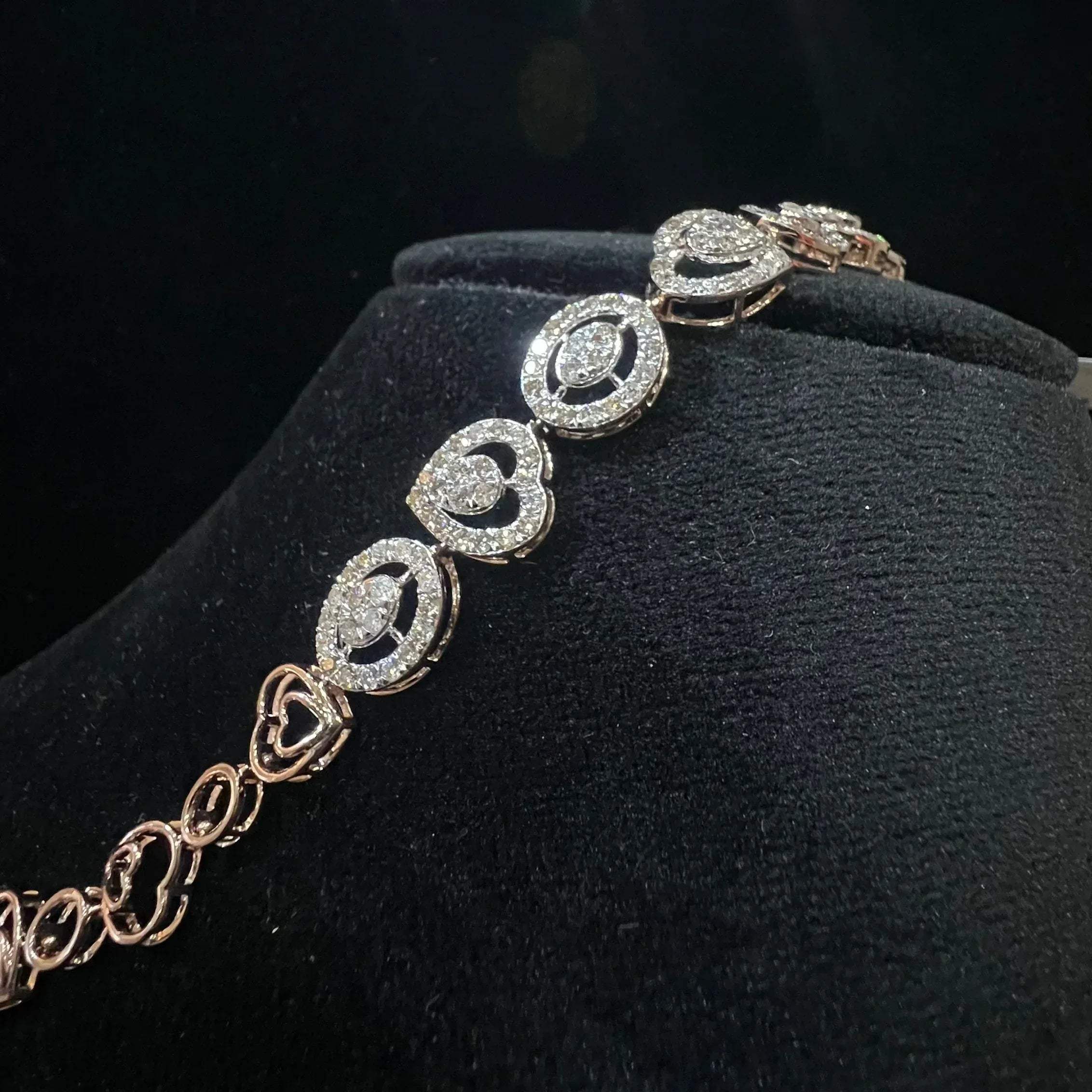 A gold diamond bracelet with oval heart shapes, displayed on a black mannequin.