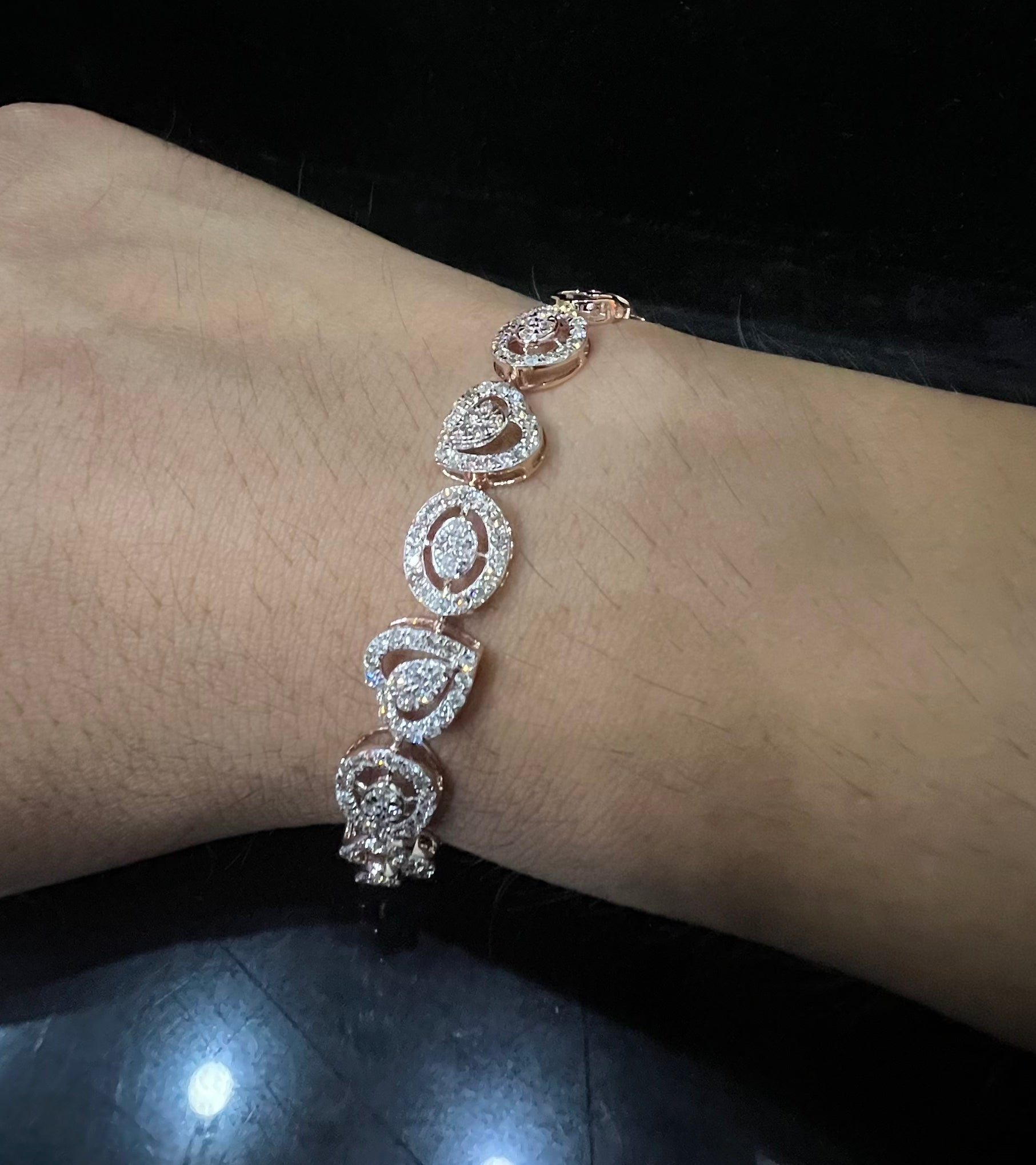 A gold diamond bracelet with oval heart shapes, displayed on a black mannequin.