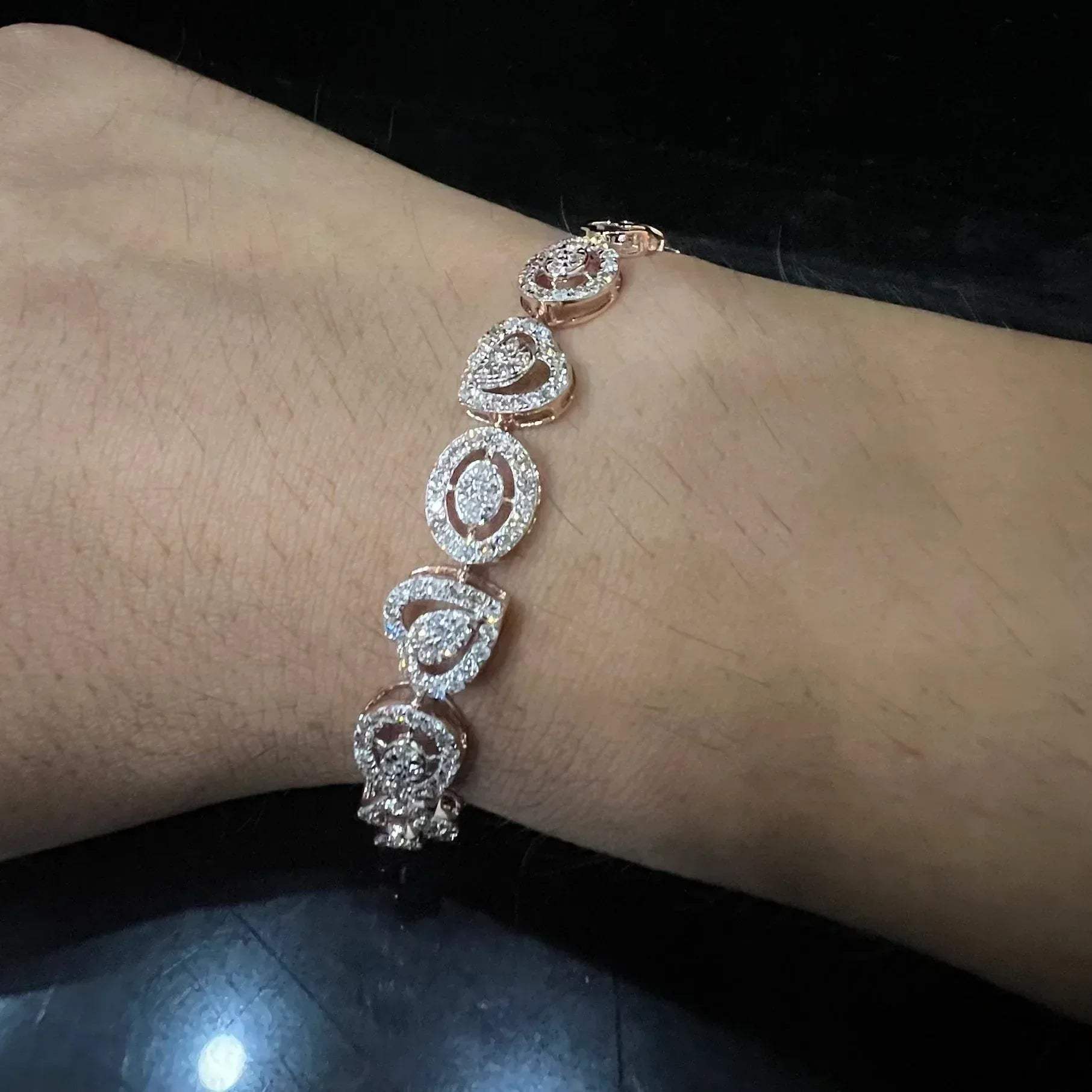 A gold diamond bracelet with oval heart shapes, displayed on a black mannequin.