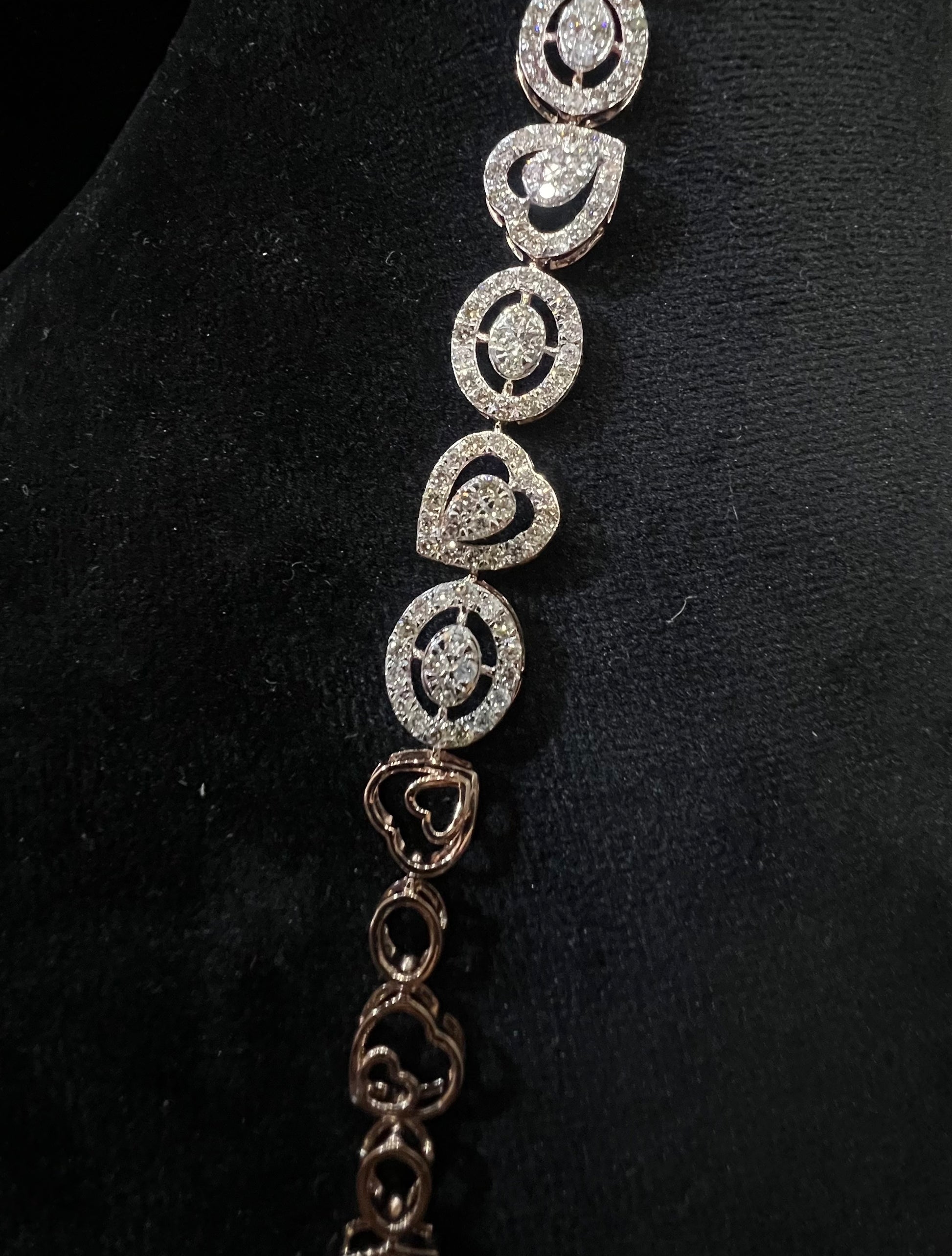 A gold diamond bracelet with oval heart shapes, displayed on a black mannequin.