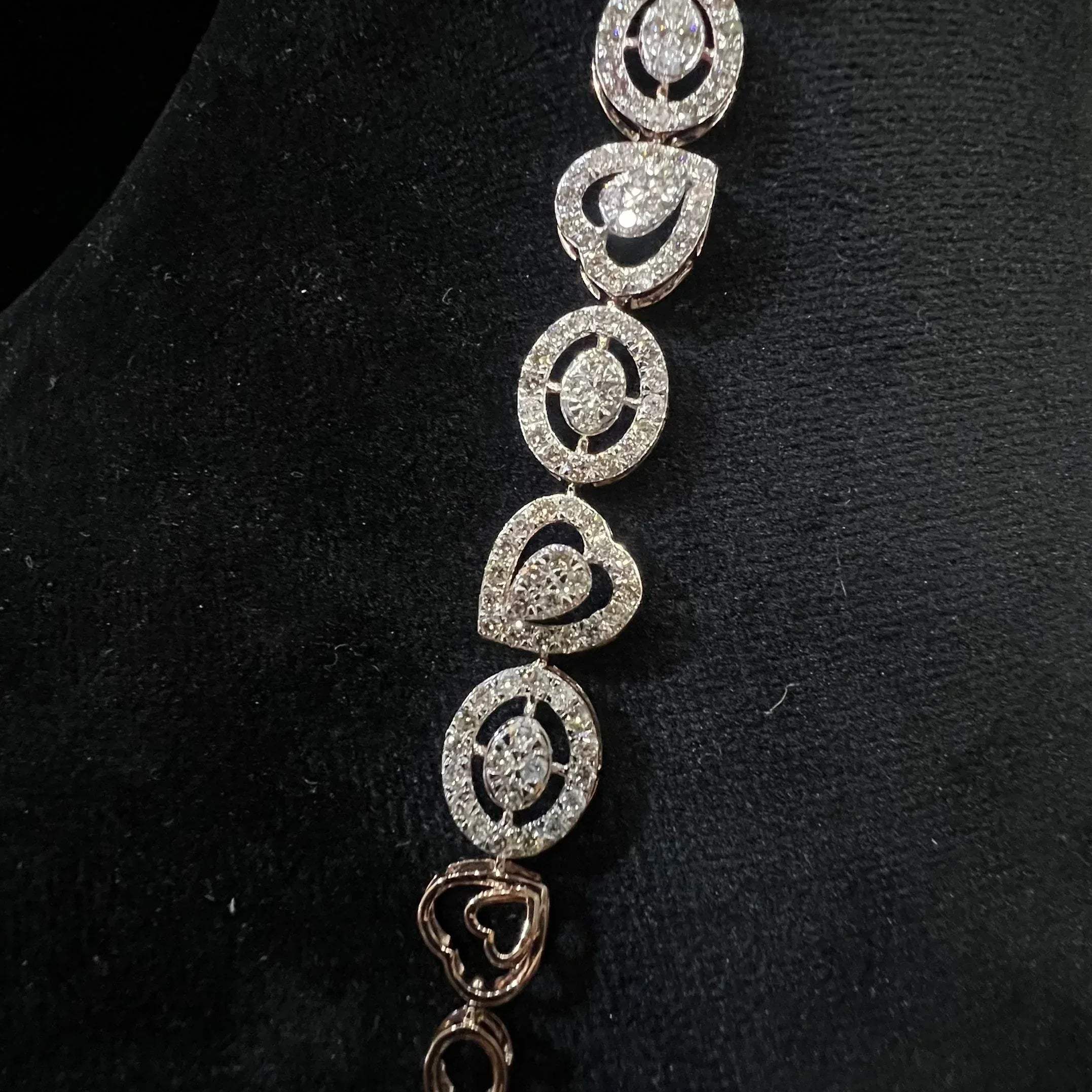 A gold diamond bracelet with oval heart shapes, displayed on a black mannequin.