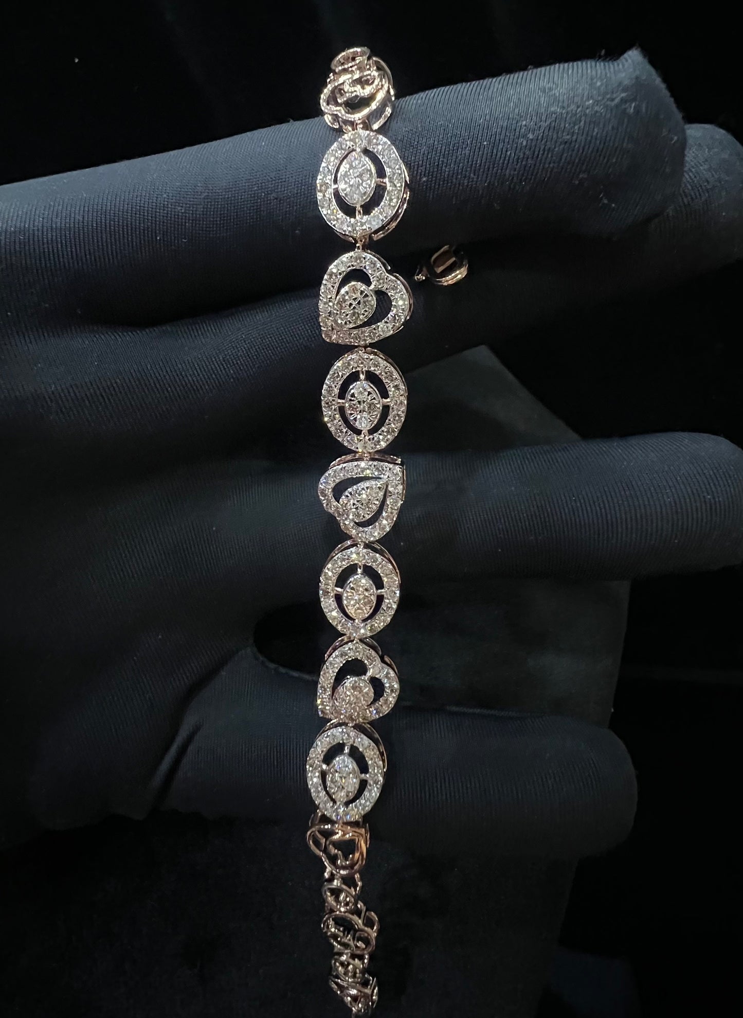 A gold diamond bracelet with oval heart shapes, displayed on a black mannequin hand.
