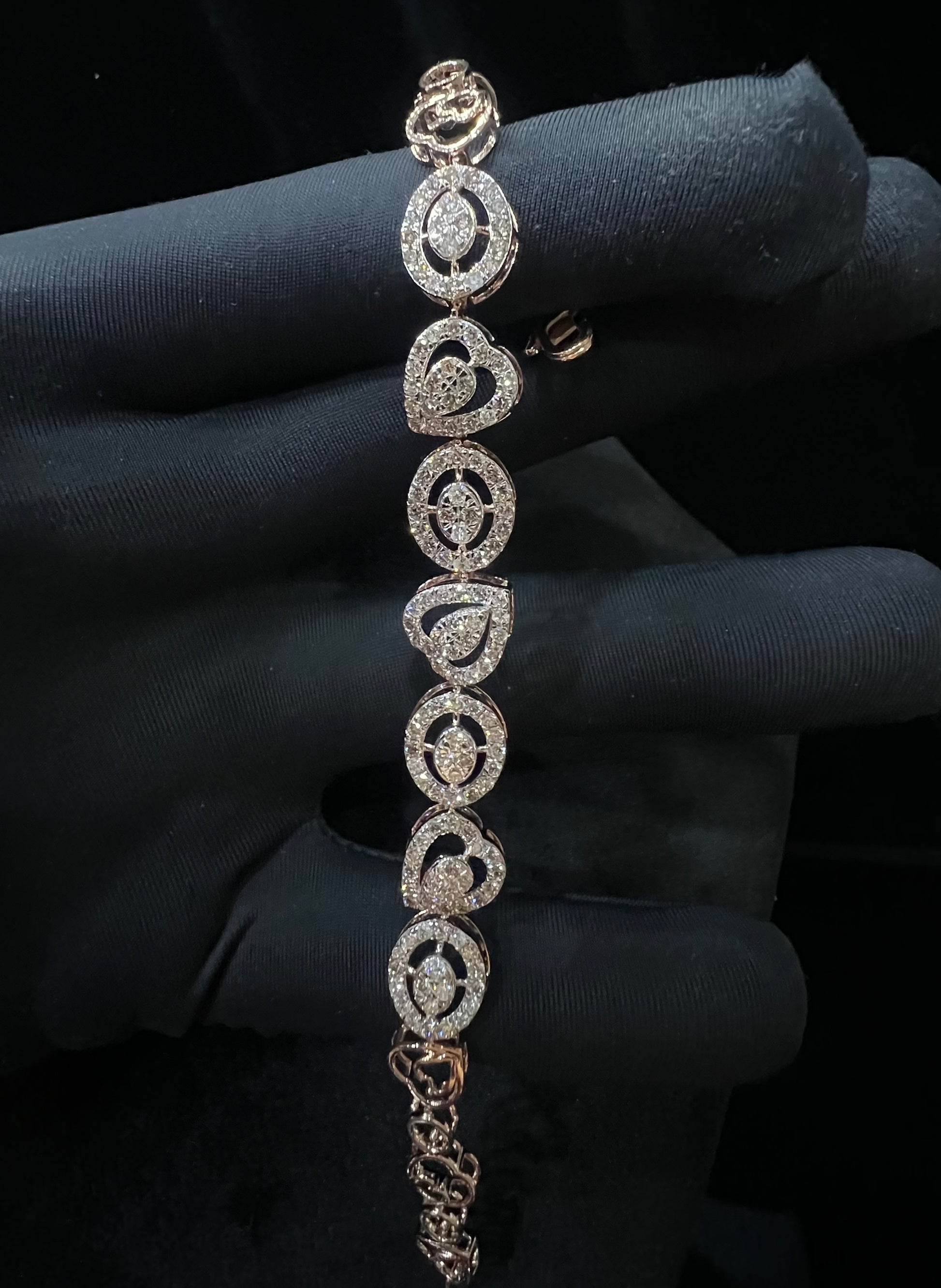 A gold diamond bracelet with oval heart shapes, displayed on a black mannequin hand.