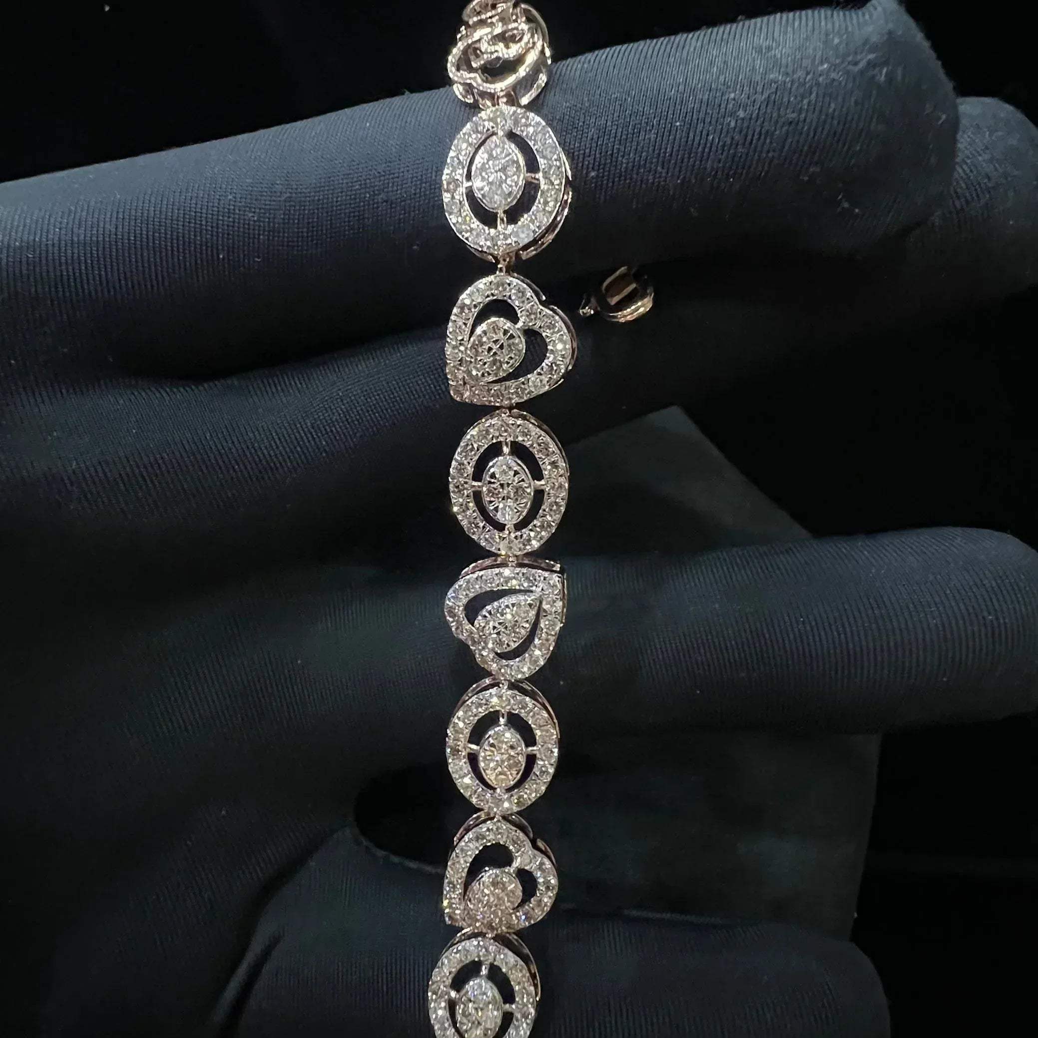 A gold diamond bracelet with oval heart shapes, displayed on a black mannequin hand.
