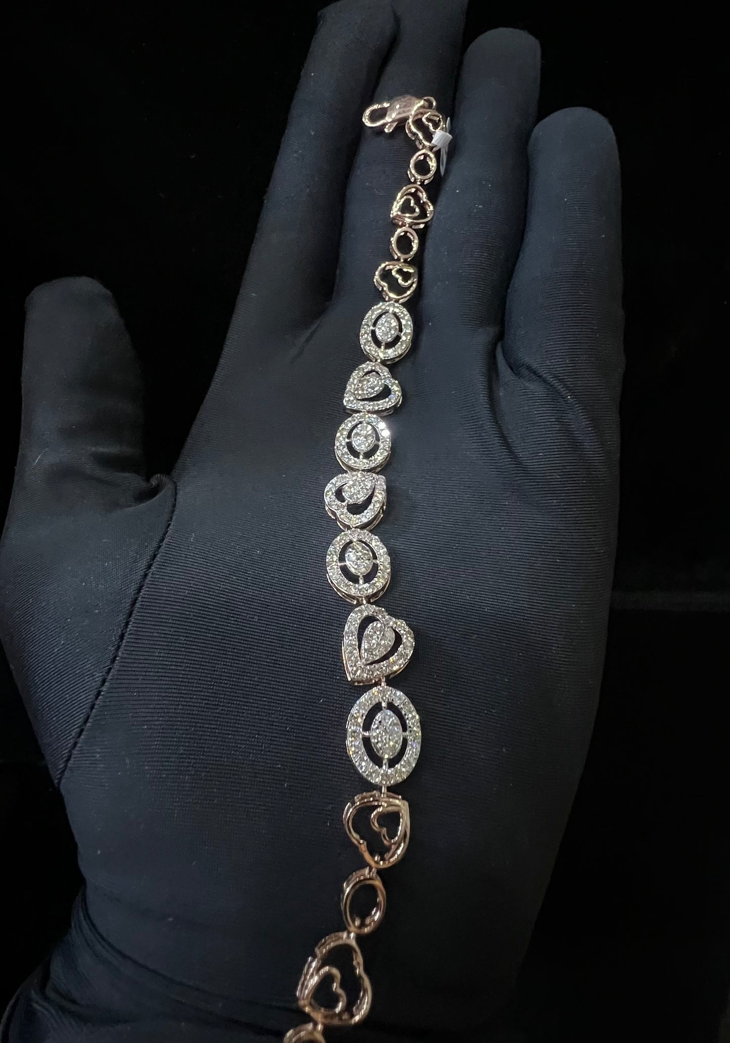 A gold diamond bracelet with oval heart shapes, displayed on a black mannequin hand.