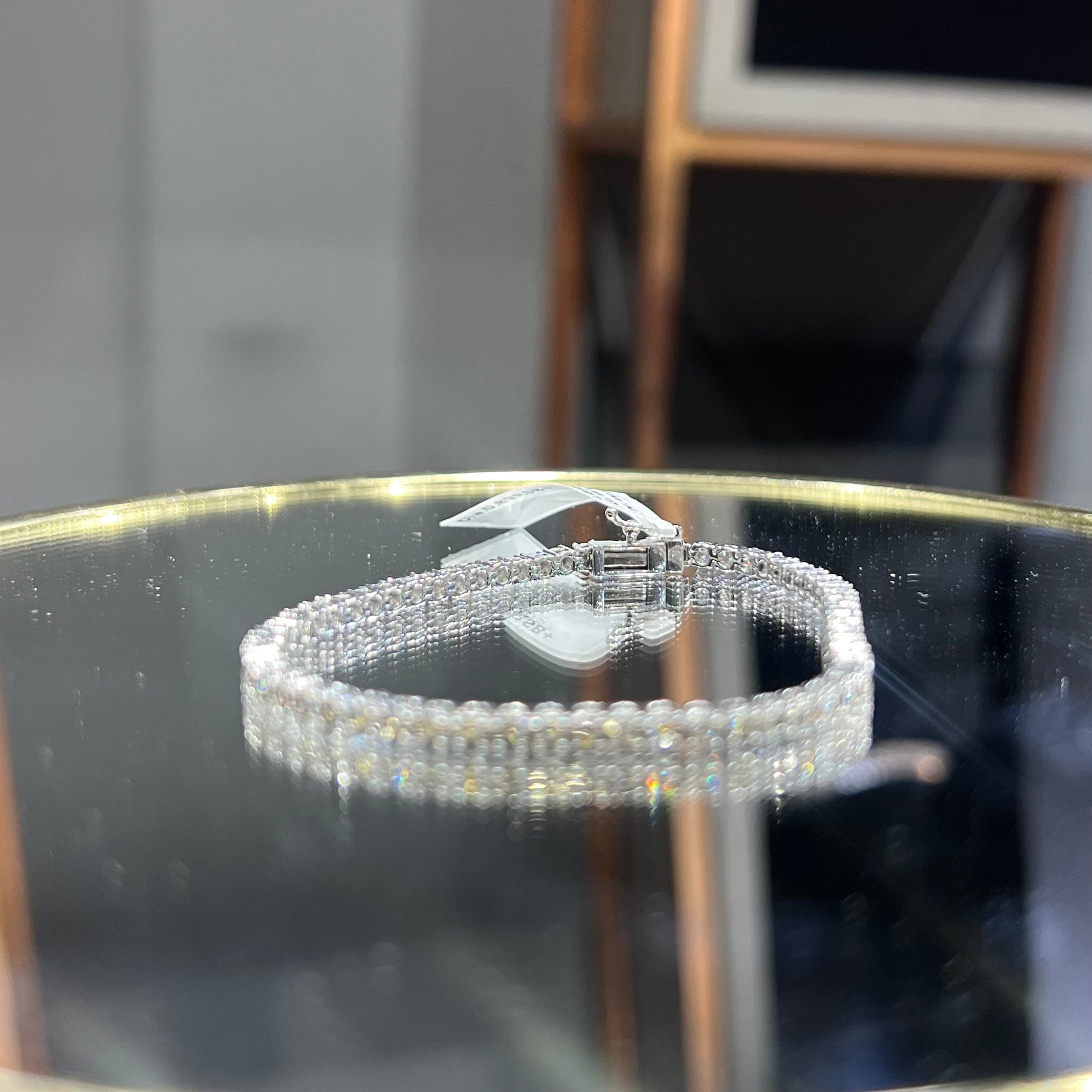 A tennis bracelet featuring a series of linked gold chains adorned with white diamonds, displayed on a glass surface.