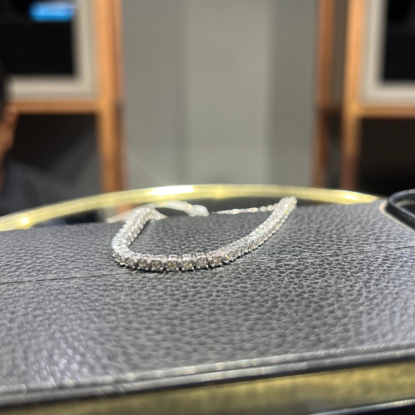 A tennis bracelet featuring a series of linked gold chains adorned with white diamonds, displayed on a glass surface.