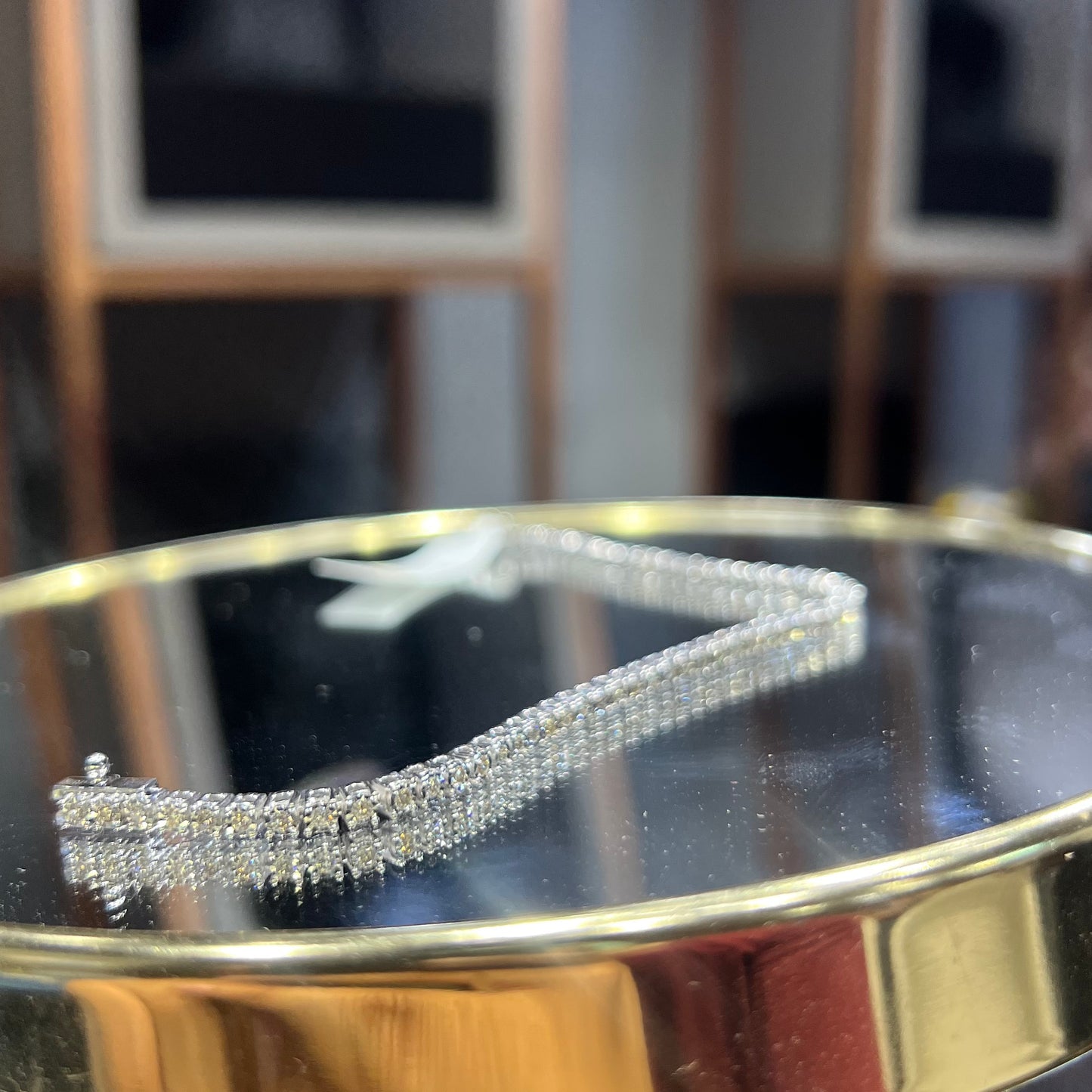 A tennis bracelet featuring a series of linked gold chains adorned with white diamonds, displayed on a glass surface.