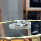 A tennis bracelet featuring a series of linked gold chains adorned with white diamonds, displayed on a glass surface.