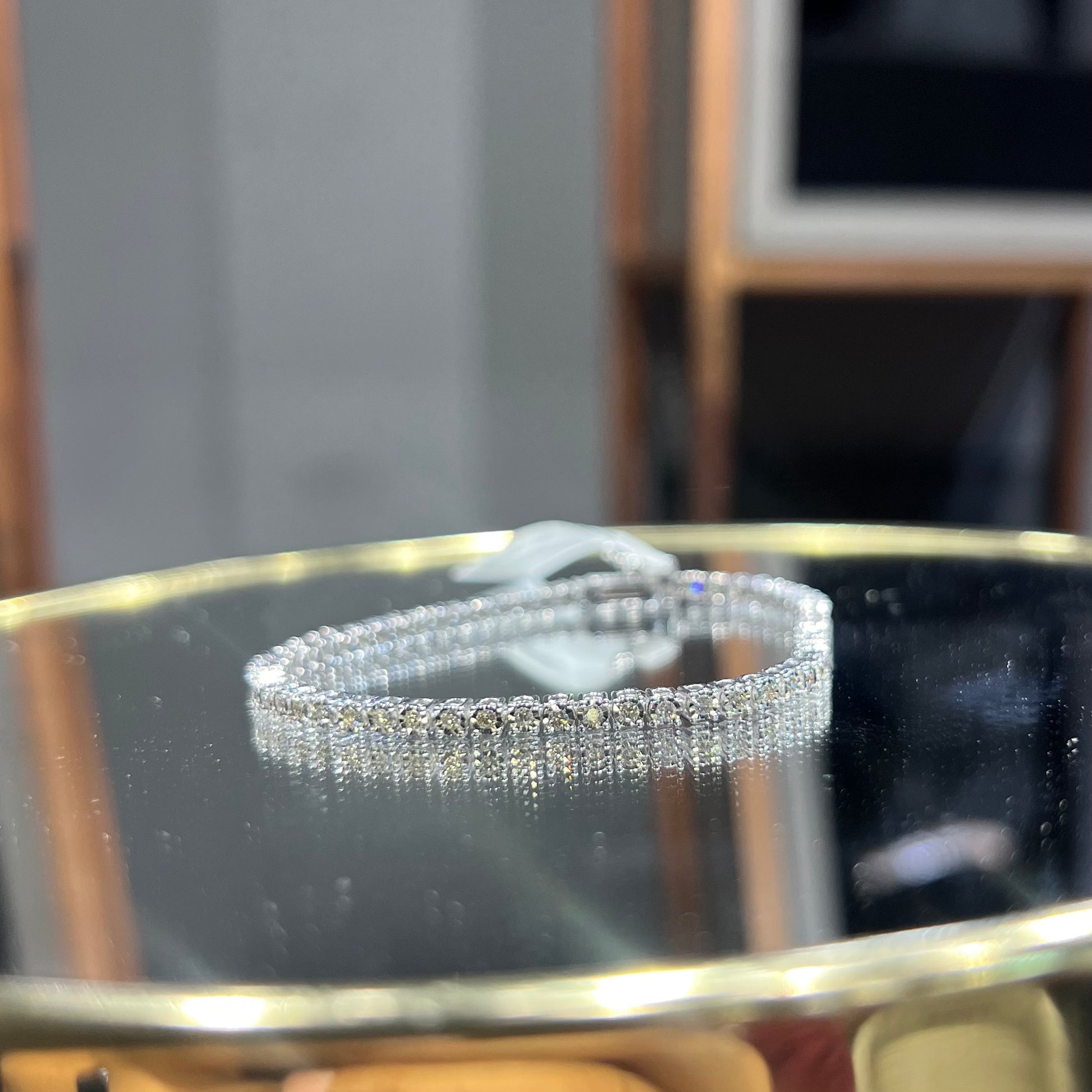 A tennis bracelet featuring a series of linked gold chains adorned with white diamonds, displayed on a glass surface.